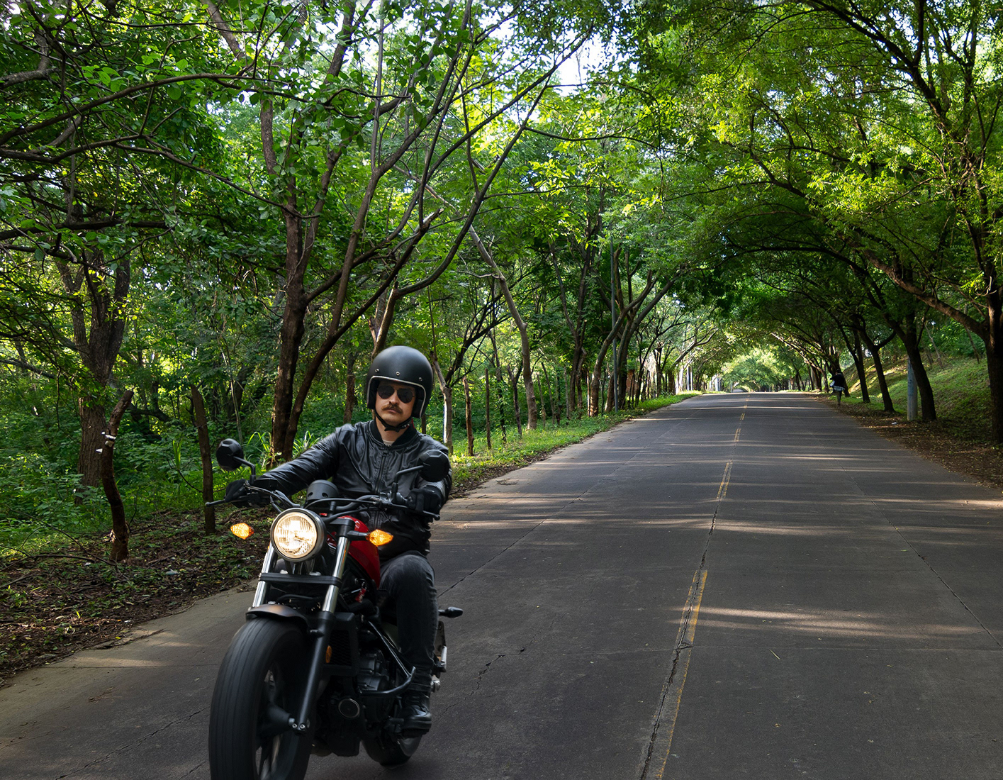 Add a man with a mustache, helmet, and sunglasses riding a motorcycle in the foreground.
