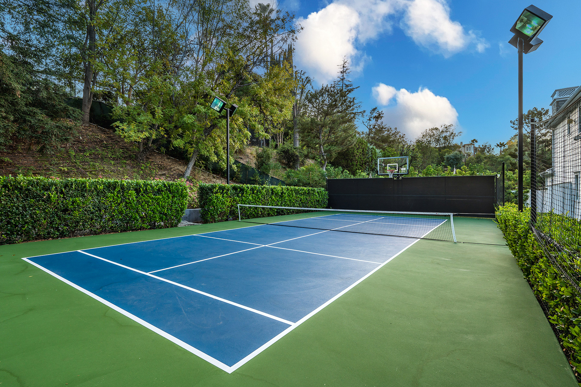 Tennis court under a bright blue sky with scattered fluffy white clouds.