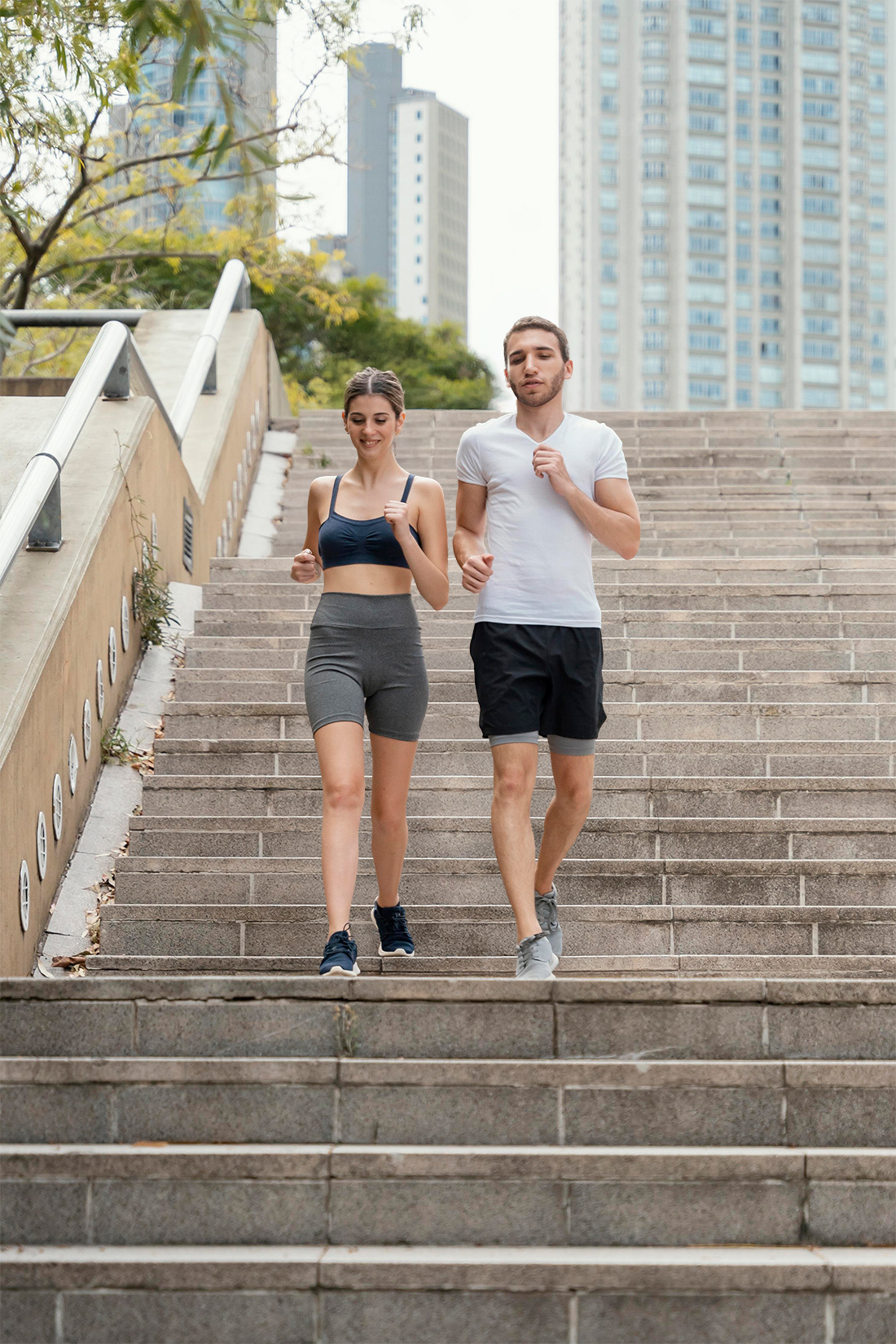 Add a man in athletic wear jogging together side-by-side down wide outdoor stone stairs in a sunny city.