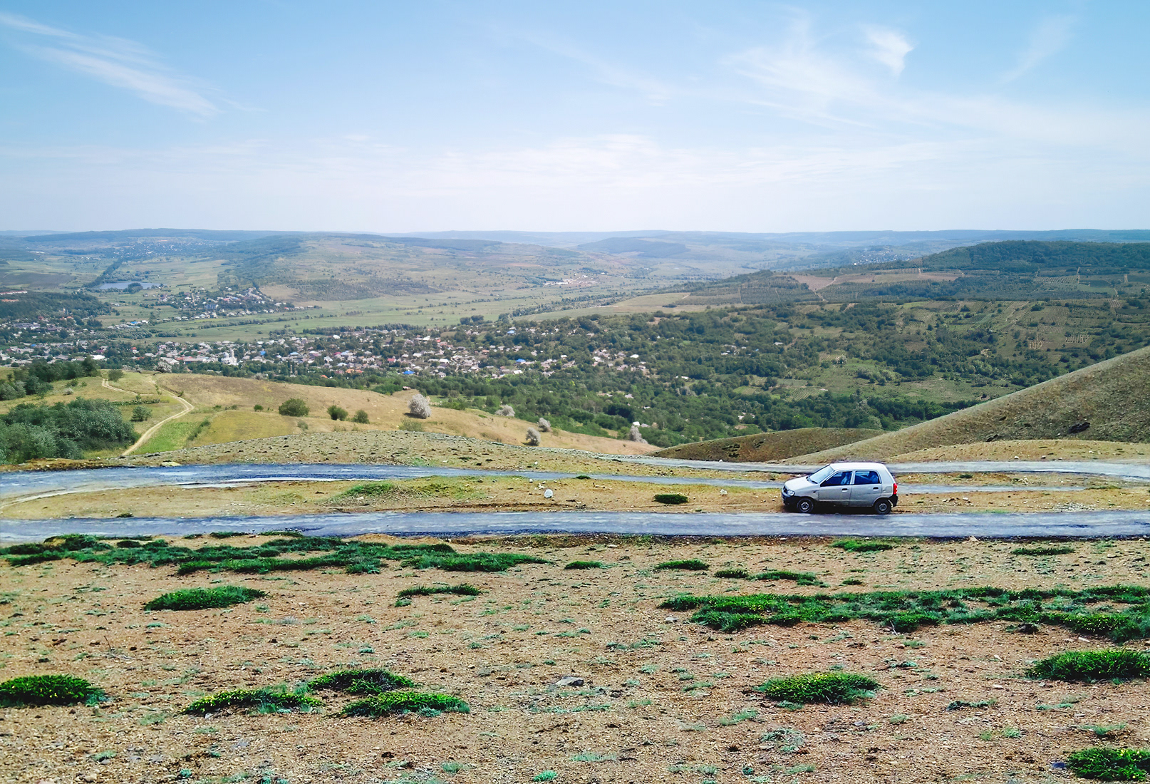 Change the foggy mountain background into a clear, sunny valley overview with distant fields, rolling hills, and a blue sky.