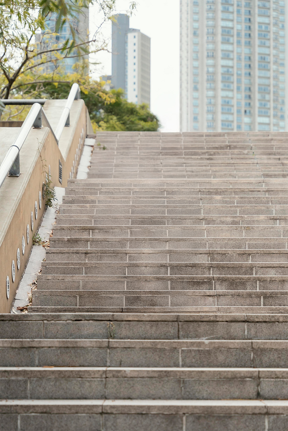 Wide shot of empty stone outdoor stairs in a city park with skyscrapers and trees in the background.