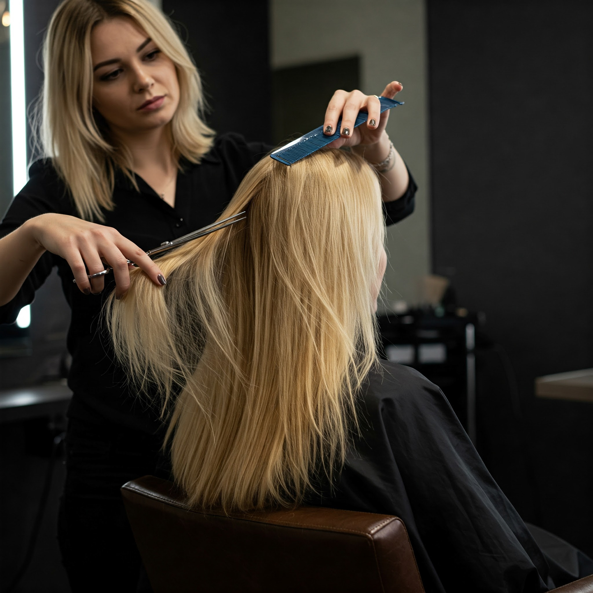 Eine blonde Friseurin schneidet die langen, blonden Haare einer sitzenden Kundin mit Schere und Kamm in einem Friseursalon.