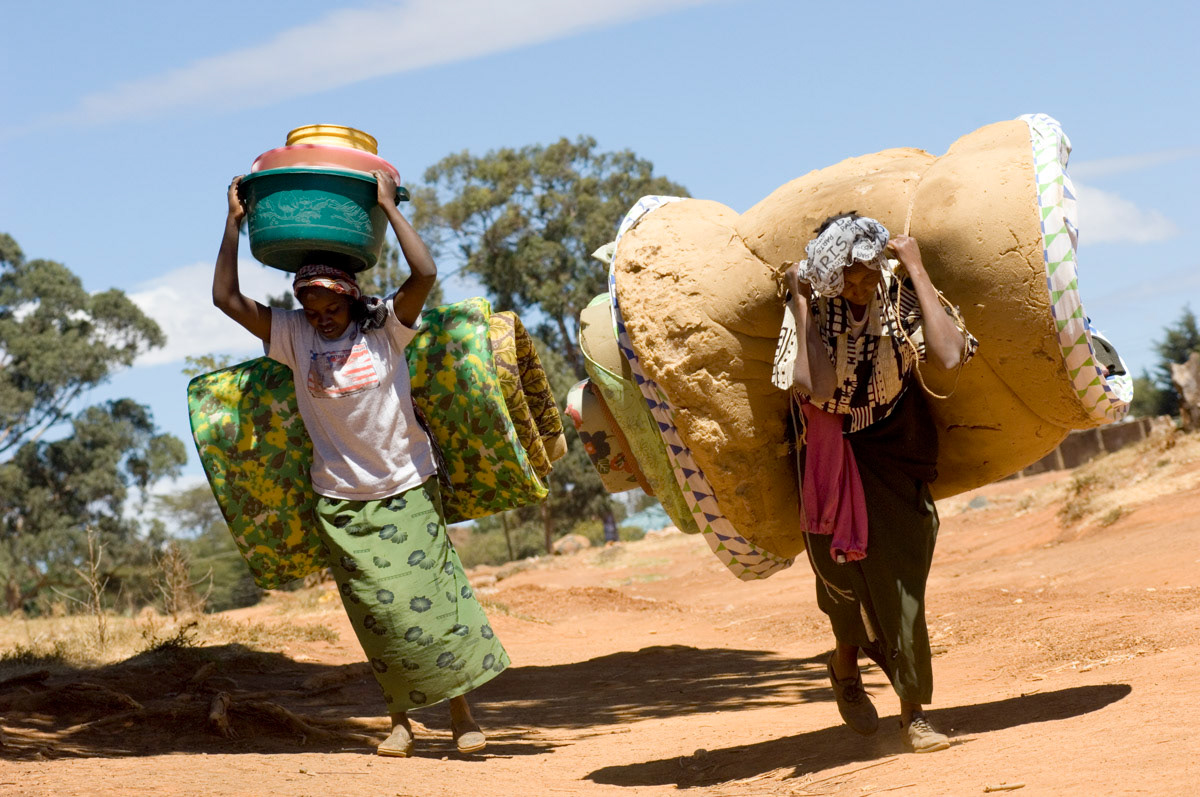 Women displaced by post election violence in Kenya, including one who fled a torched church where at least 18 people died, carry belongings to a place of refuge.