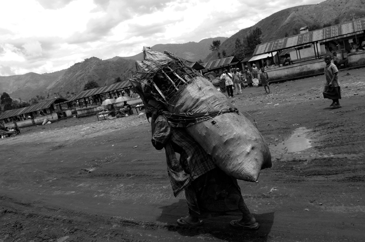 An elderly lady carries a heavy load of charcoal to the market in Sake, near Goma. Many women are attacked when carrying out their daily activities such as traveling to the market to sell produce