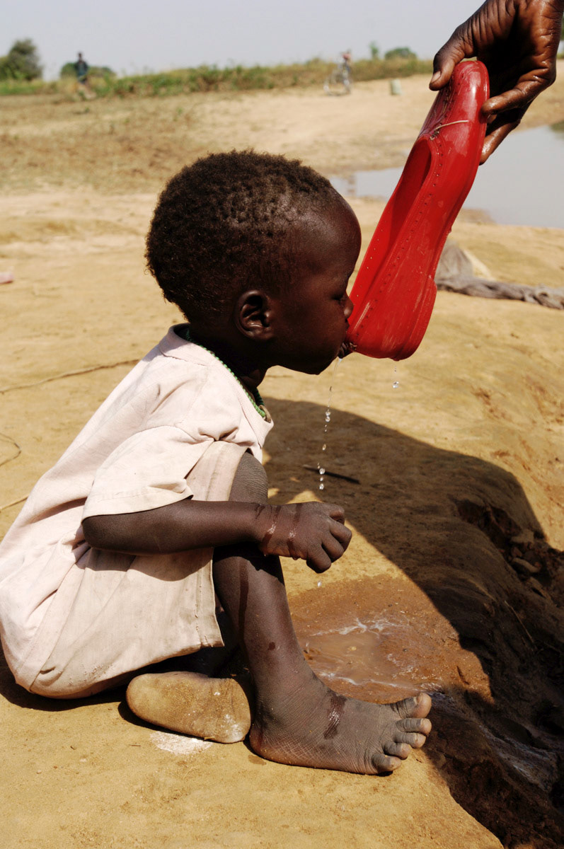 A mother gives her thirsty child a drink by the Aquem river, Southern Sudan.