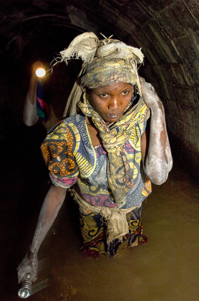 Dorica Biwaga, 25, waist deep in water, carries 30 kgs of rocks out of Makala gold mine, after six hours inside. Her sister, Emanuella, 40, follows behind. They crawled for three hours, through tunnels so narrow that at one stage Dorica got stuck. Dorcia, a widow and mother of two, started this work in 1996. Her body is in constant pain from the work, and her periods irregular.