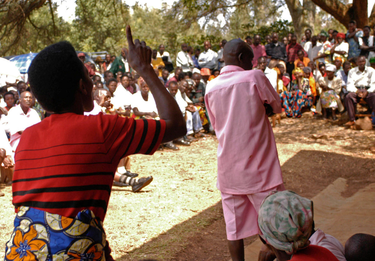A community member speaks out at a Gacaca court session, Rwanda. During the hearing the accused (eight on this day, dressed in pink) face the community where they committed the atrocities during the 1994 genocide and speak in detail of their crimes as survivors witness and respond to the statements. August 2005.