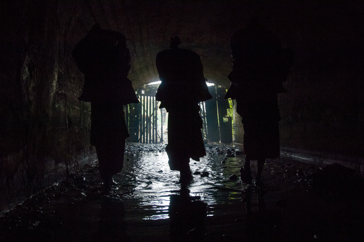 Three women carry bags of charcoal into Adidi mine, which will be burnt to assist in breaking the rocks. This depletes the oxygen levels in the mine creating a serious health risk.