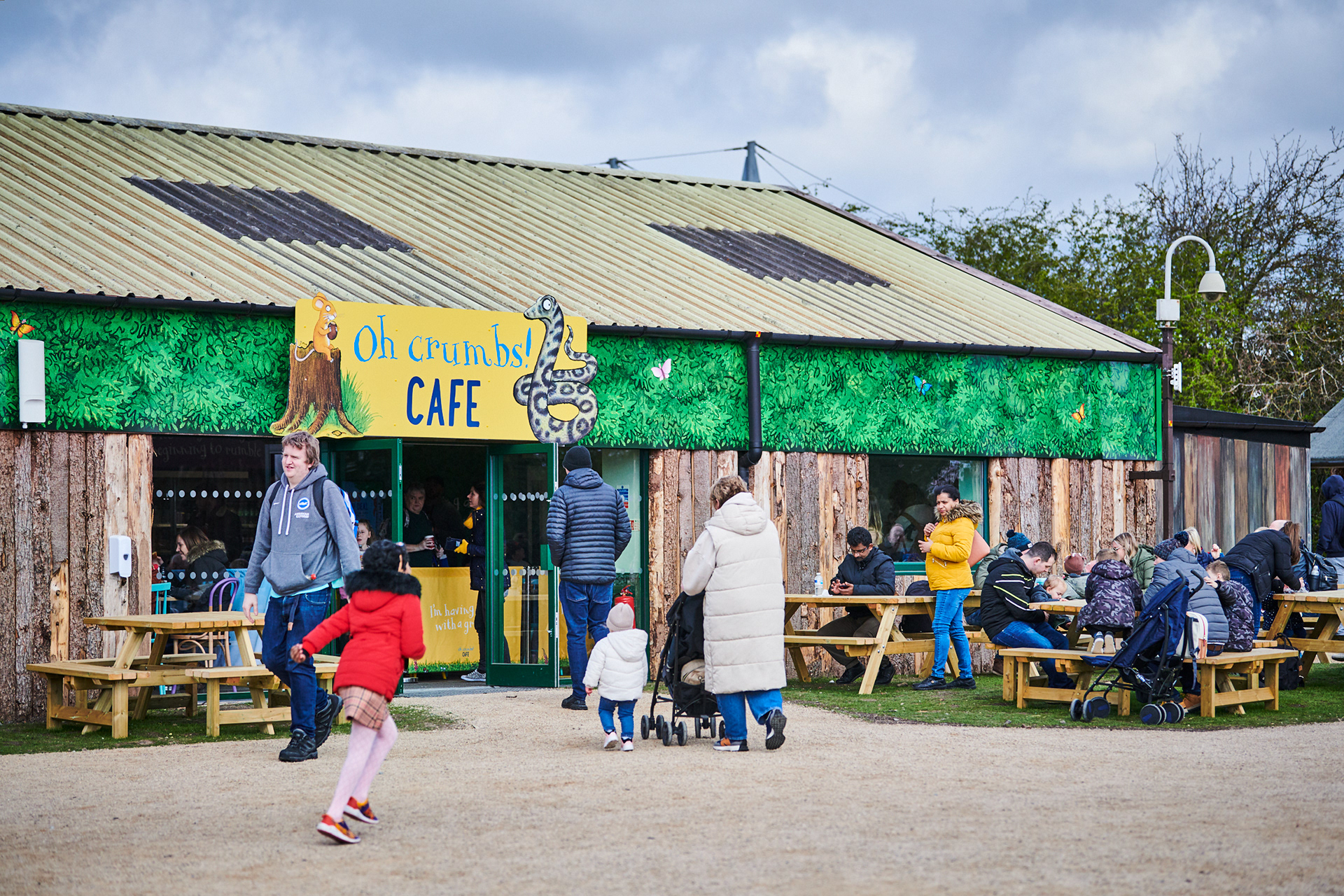 Oh Crumbs! Cafe - Outside themed with a large offset sign with background foliage
