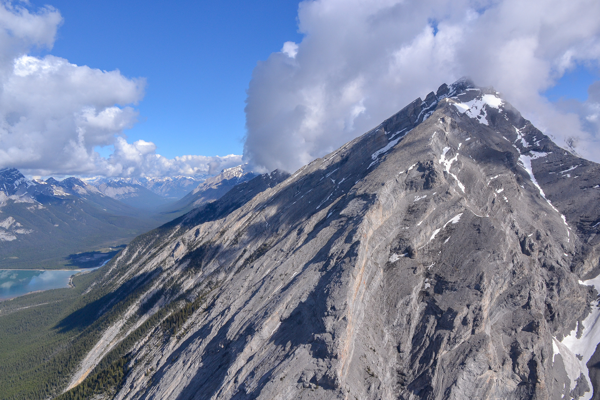 The stark, bare grey rockface of the Canadian Rocky Mountains rise high above the vegetation line.