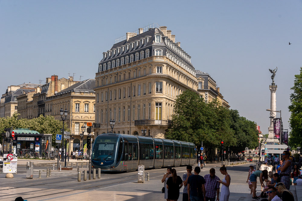 An e-tram cruises past Conseil Interprofessionnel du Vin de Bordeaux with Lady Liberty atop Monument aux Girondins in the background.