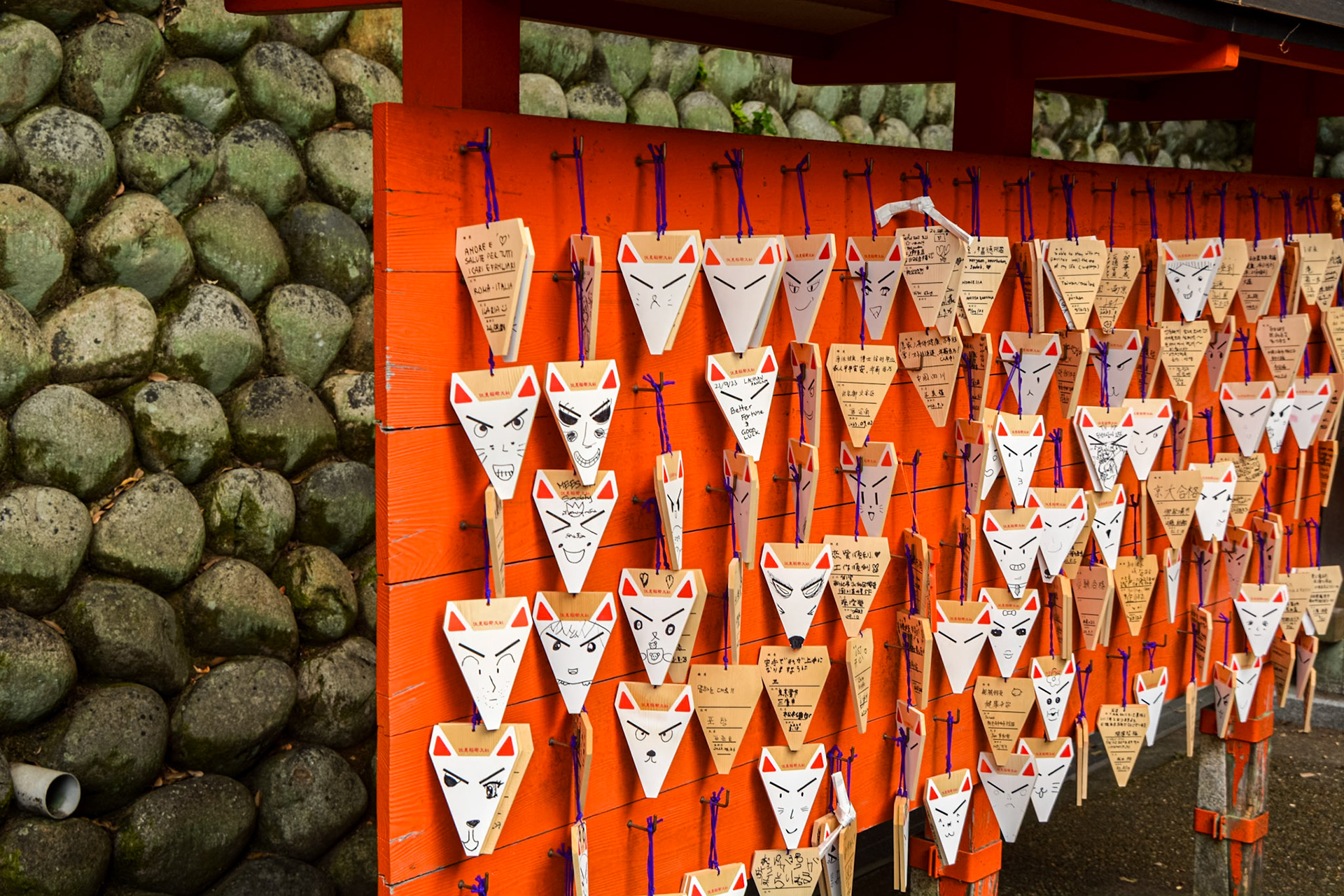 Fushimi Inari - Omokaru-ishi (Stone of fortune telling) messages hanging of good fortune hanging from a wall.