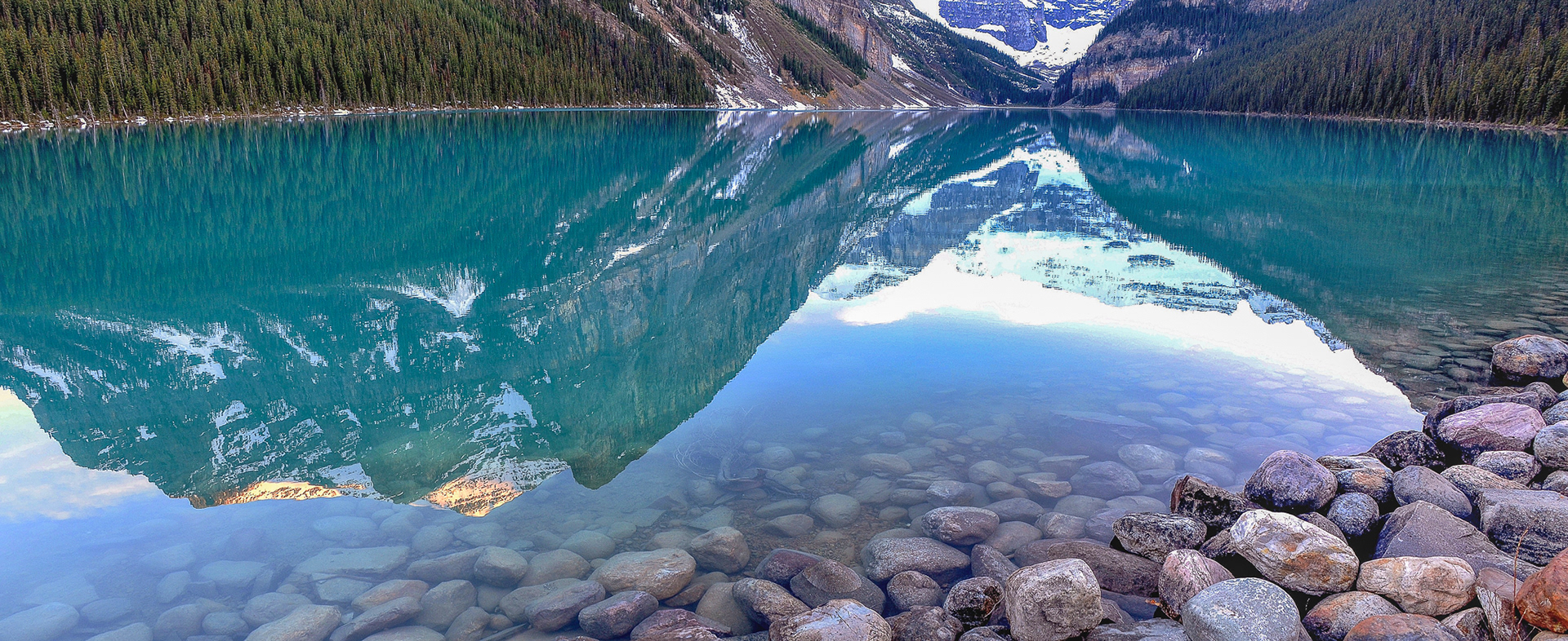 Boulders on the lake bed recede into the depths of Lake Louise amid the reflections.