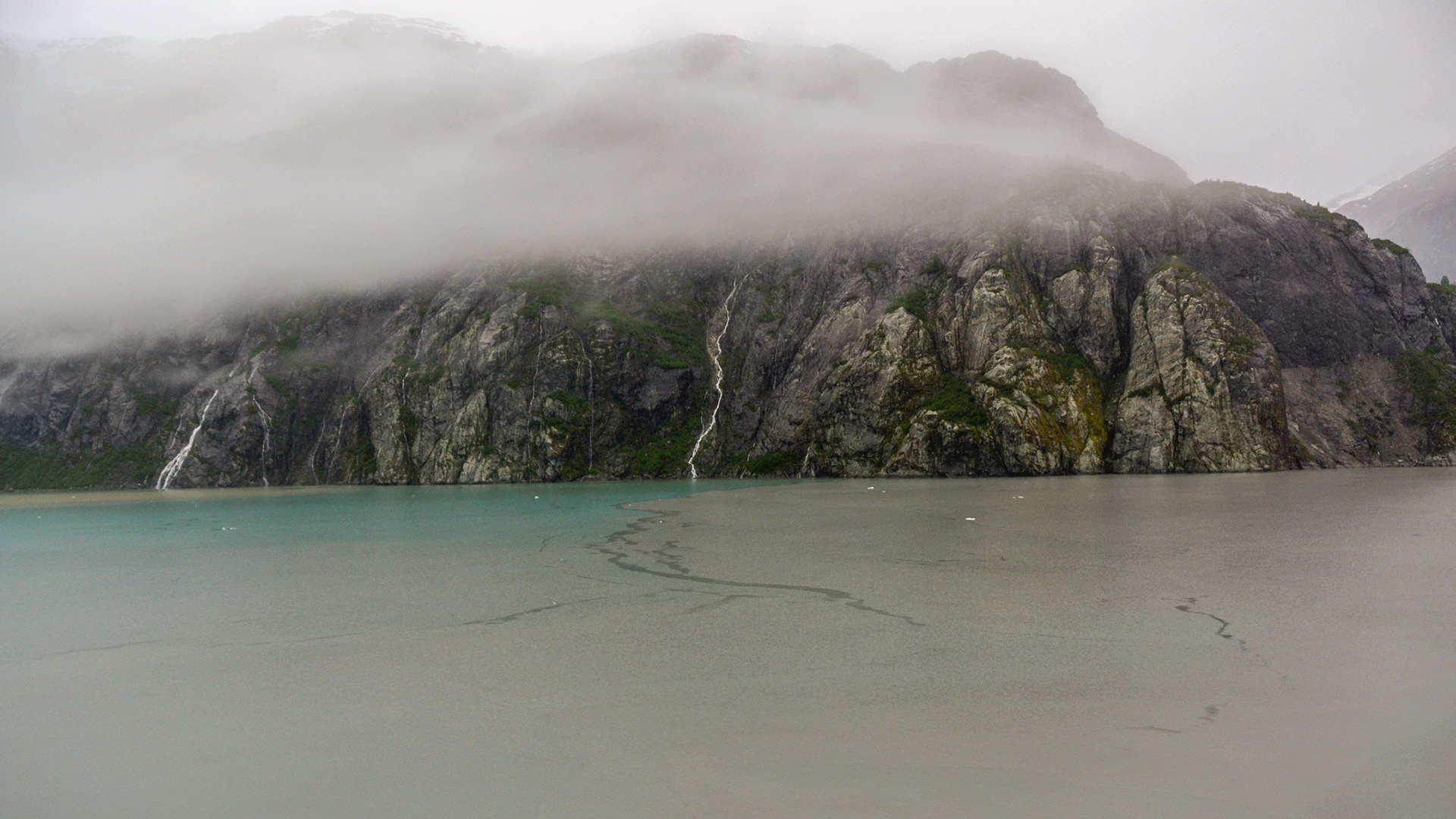 Low cloud and mist shroud the rocky shoreline.