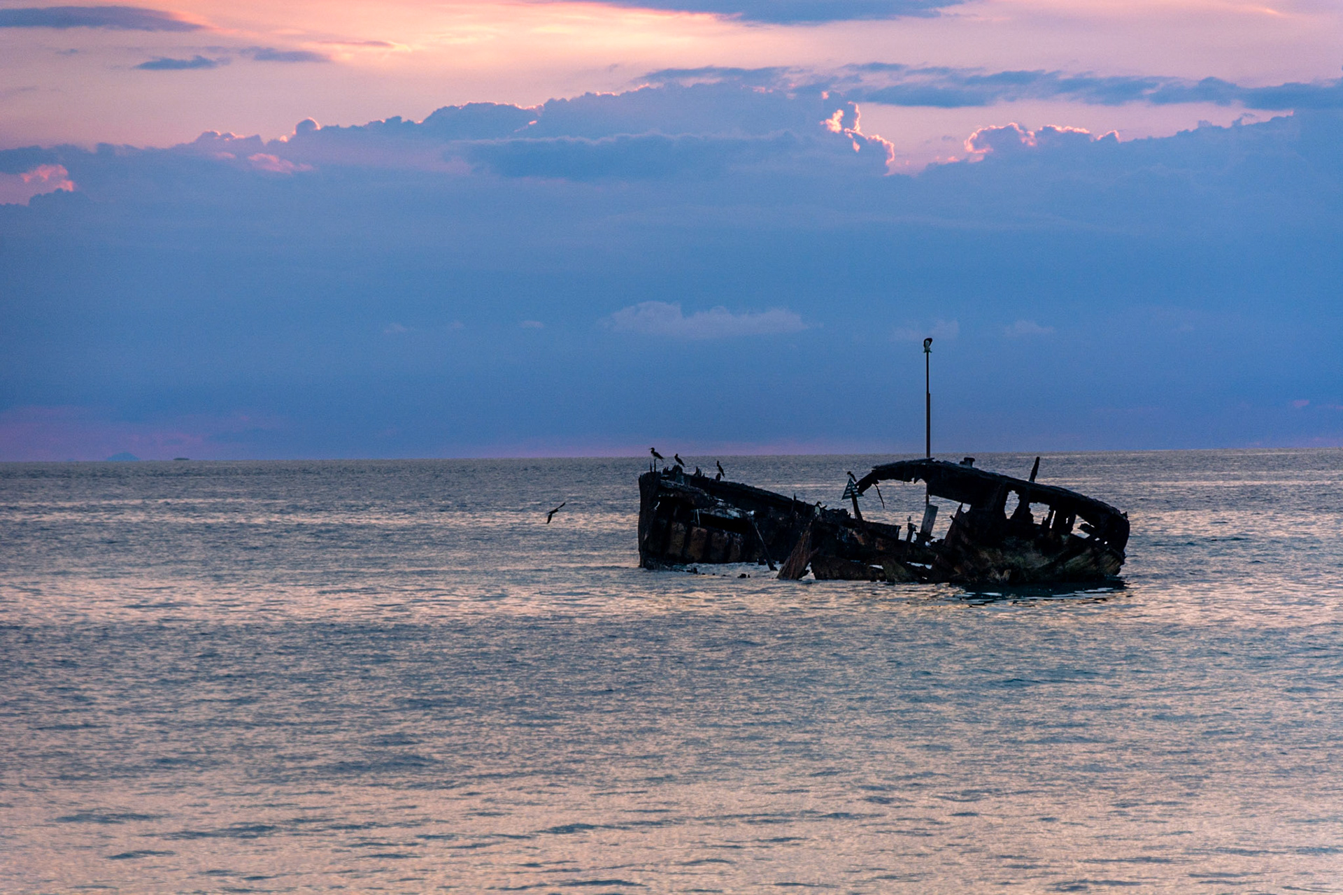 The rusting remains of HMAS Protector silhouetted against the dark clouds.