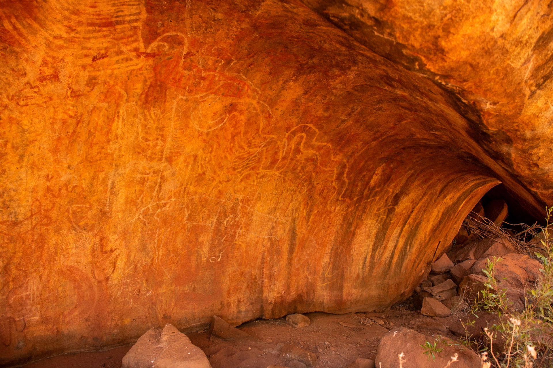Rainbow serpent artwork adorns the wall of an overhanging cave