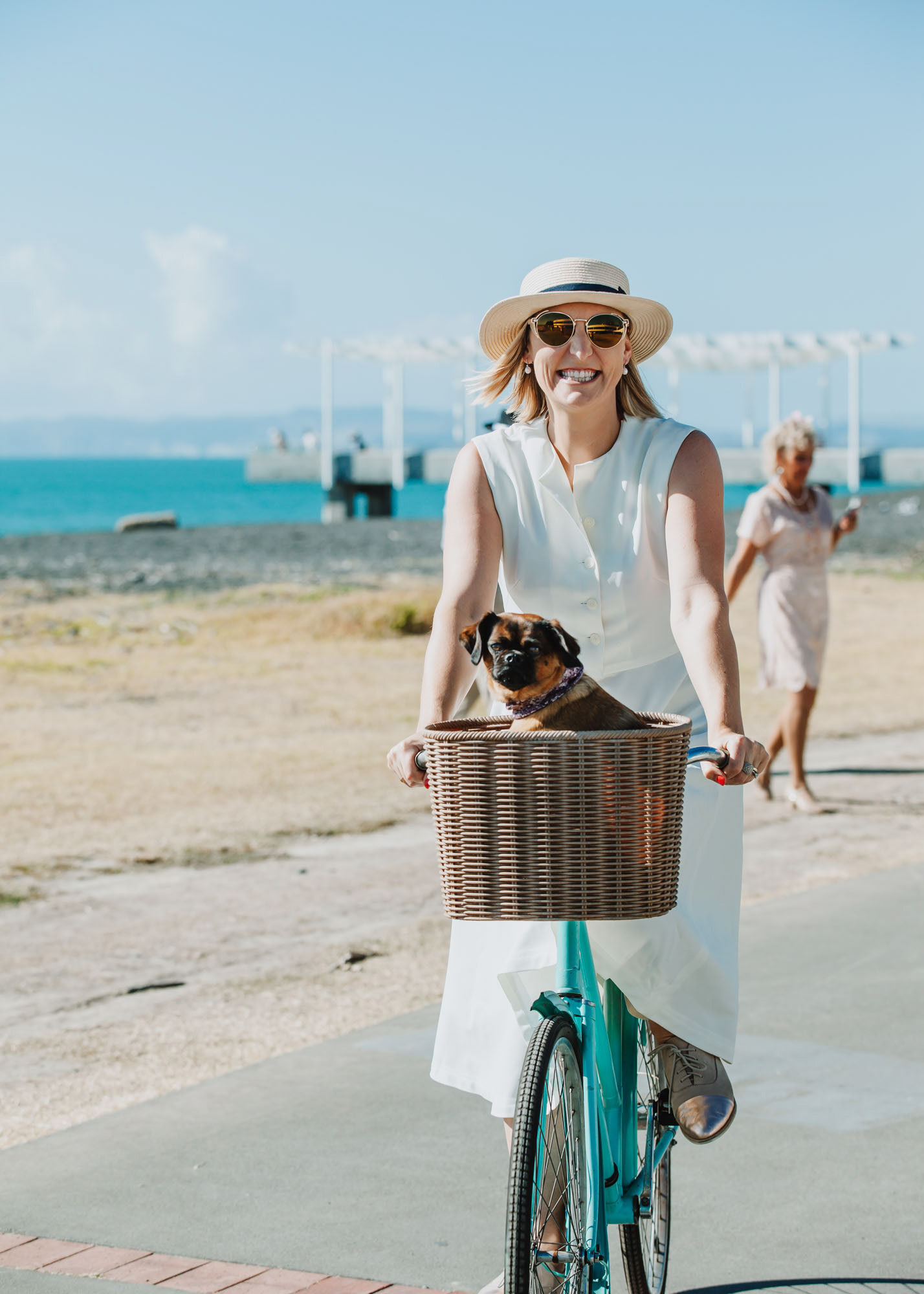 Smiling woman in Art Deco costume riding her bike with dog in basket