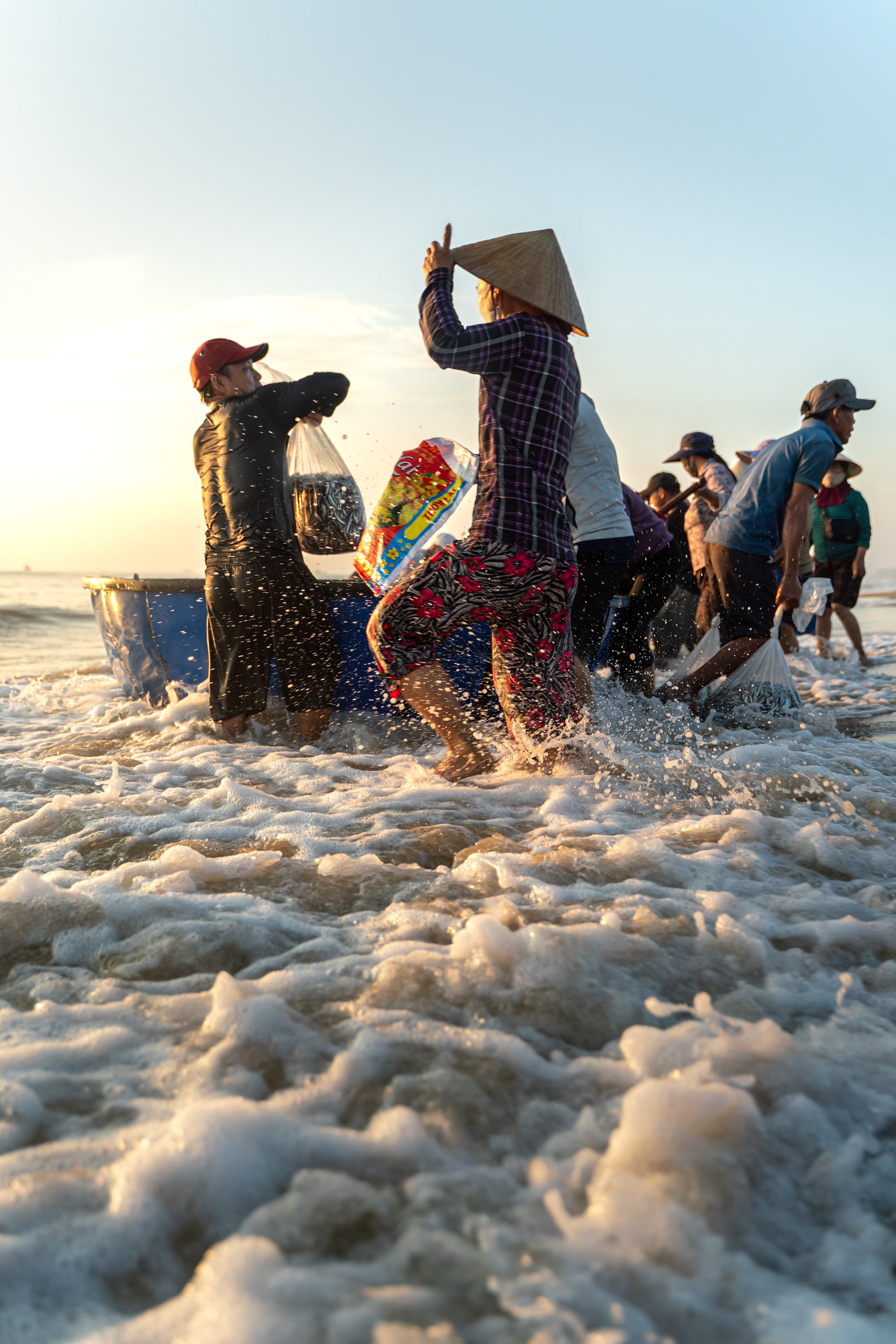 People wading through waves to collect fish from returning boats near Hoi An.