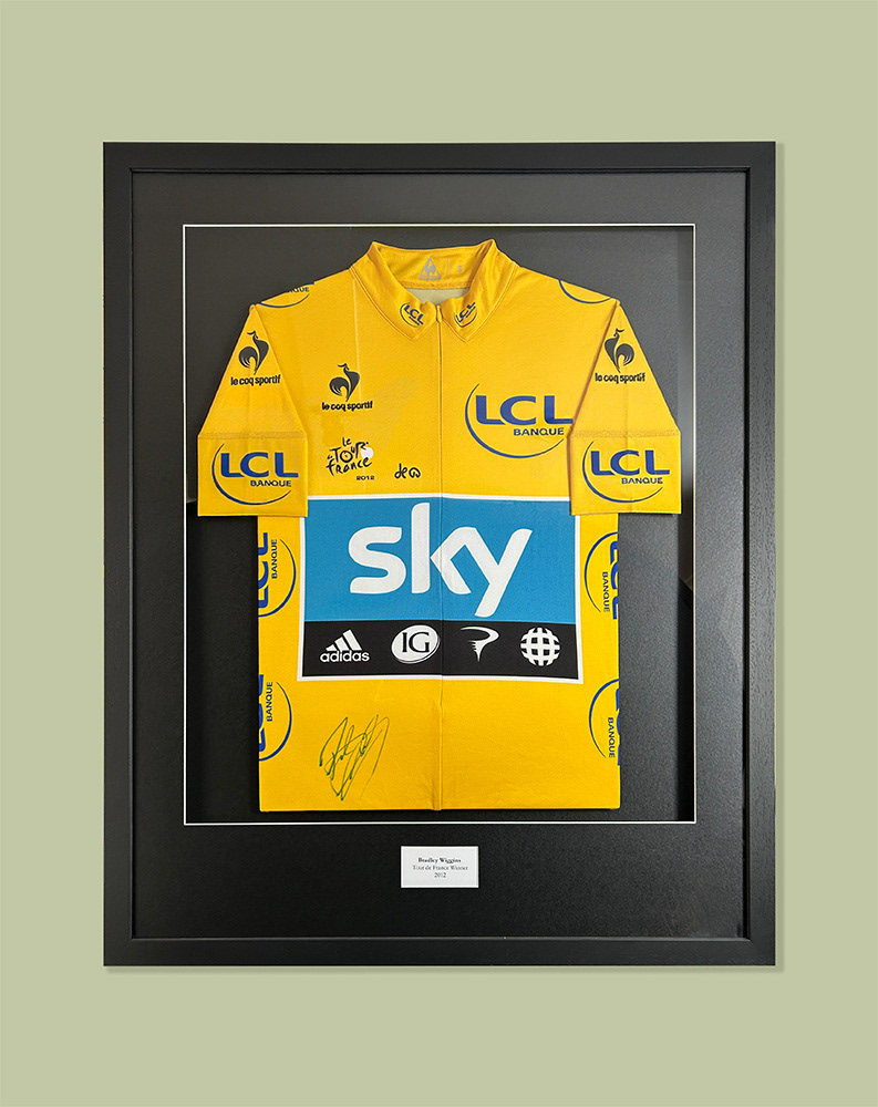 Signed Bradley Wiggins Cycling Jersey framed with sleeves visible on black mountboard and black woodgrain moulding. Framed using conservation methods so fully reversible.