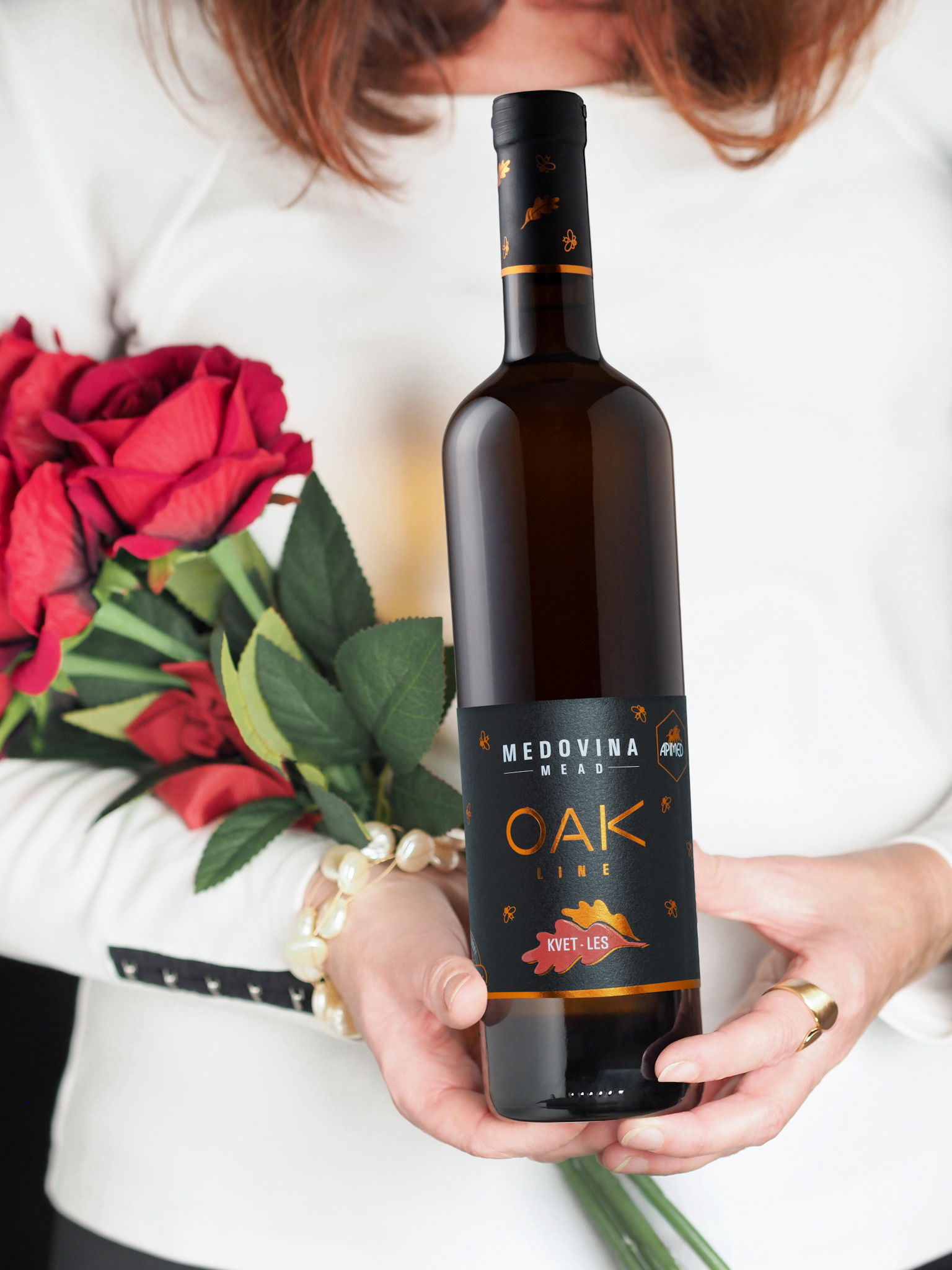 Žena v bielom s červenými ružami a fľašou medoviny Apimed - autor Jana Kollarova