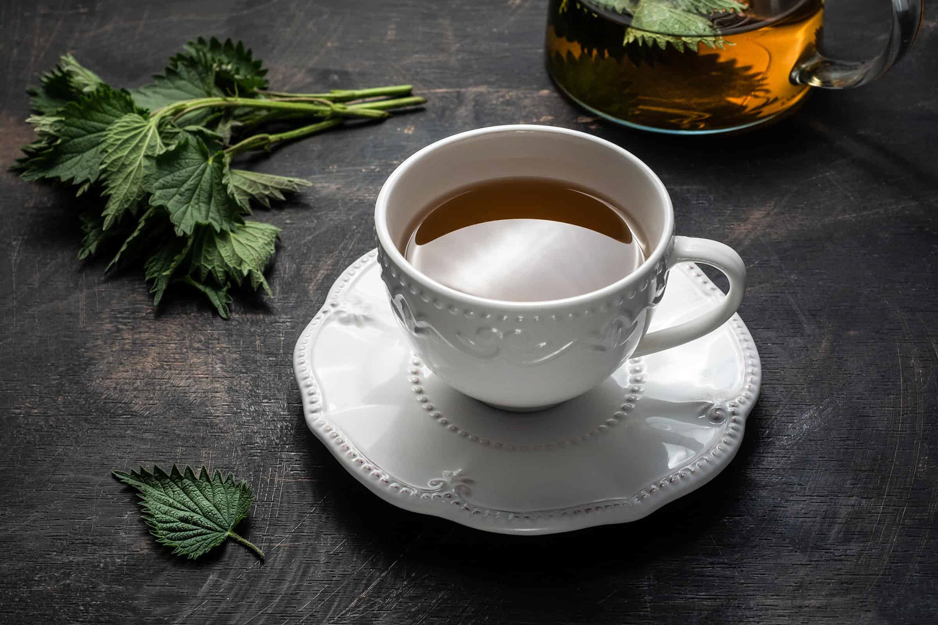 Biela šálka so žihľavovým čajom na tmavom podklade. Šikmý pohľad zhora. Autor Jana Kollarova.