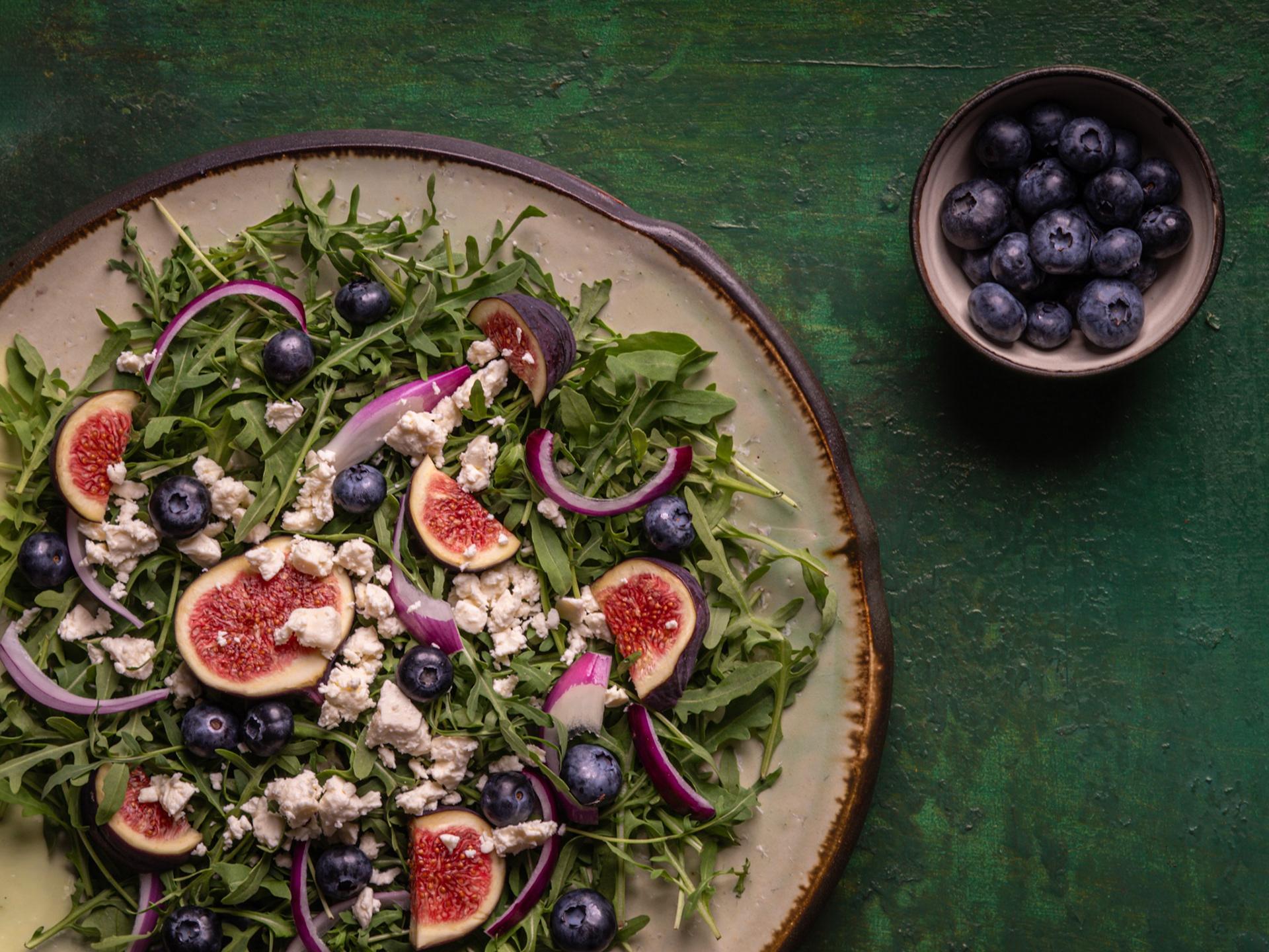 Rukolový šalát s figami, čučoriedkami a fetou na zelenom pozadí. Pohľad zhora. Autor Jana Kollarova