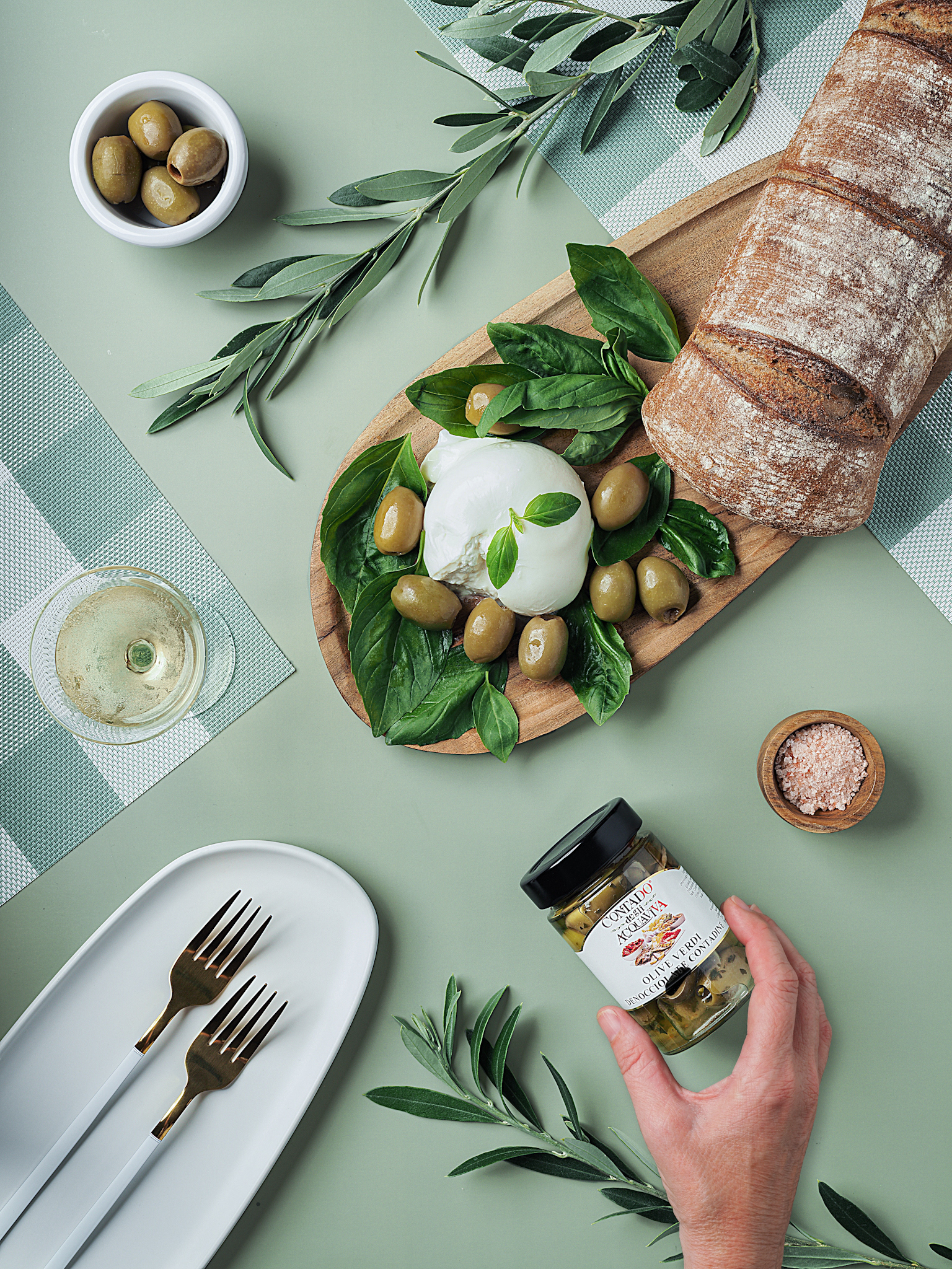 Nakladané olivy, burrata, čerstvá chlieb a pohár vína na zelenom podklade. Pohľad zhora. Autor Jana Kollarova