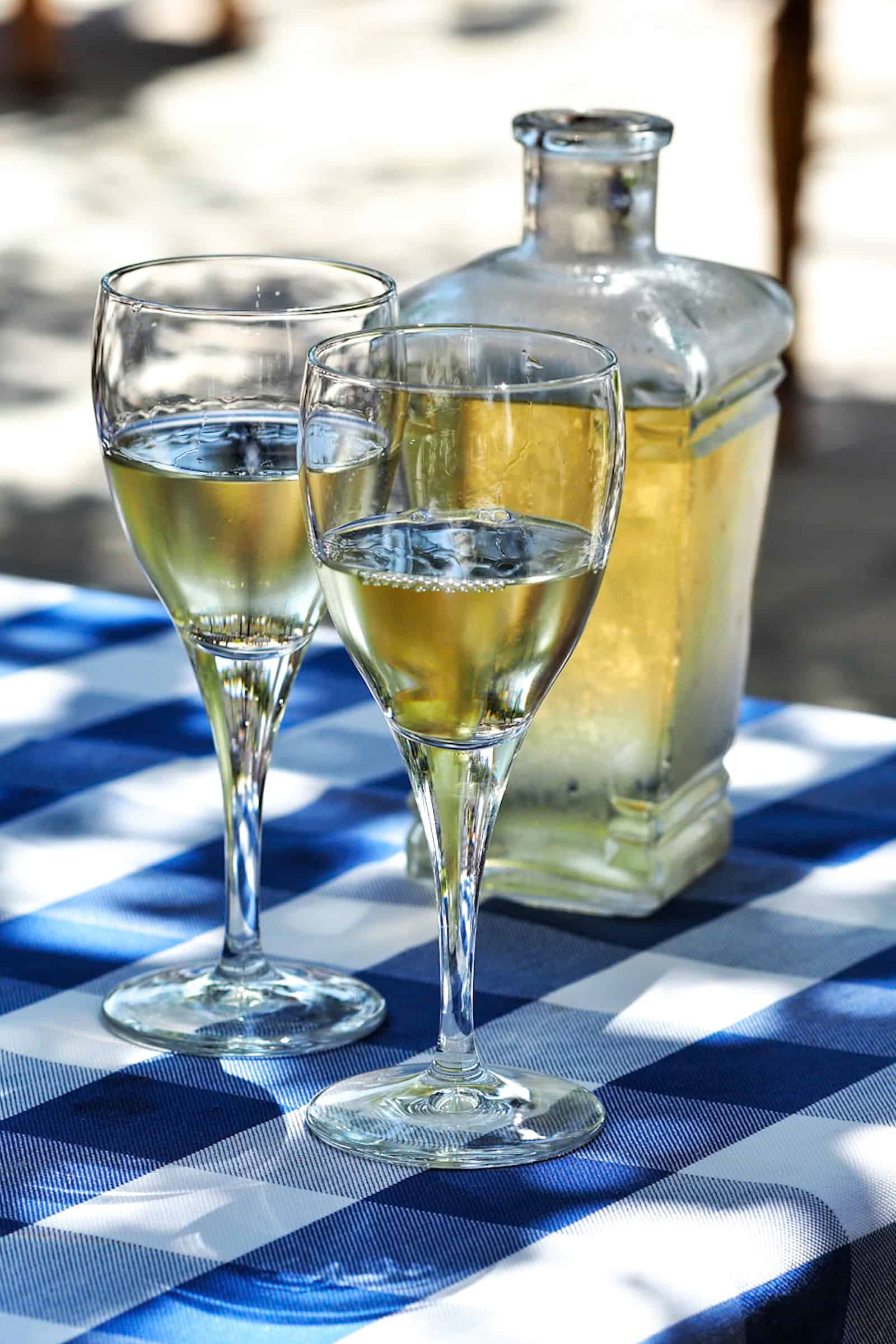 Fľaša bieleho vína a dva poháre na stole s bielo-modrým obrusom. Pohľad spredu. Autor Jana Kollarova.