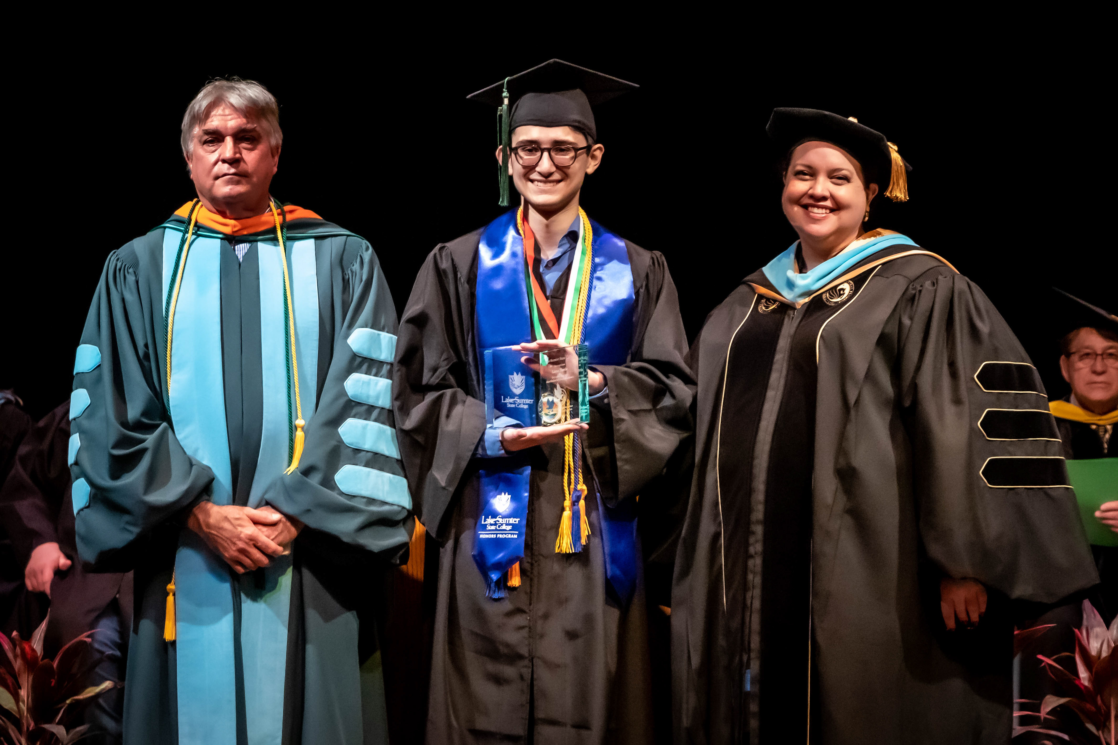 On stage at graduation with the President and Vice President of Enrollment & Student Affairs at graduation
