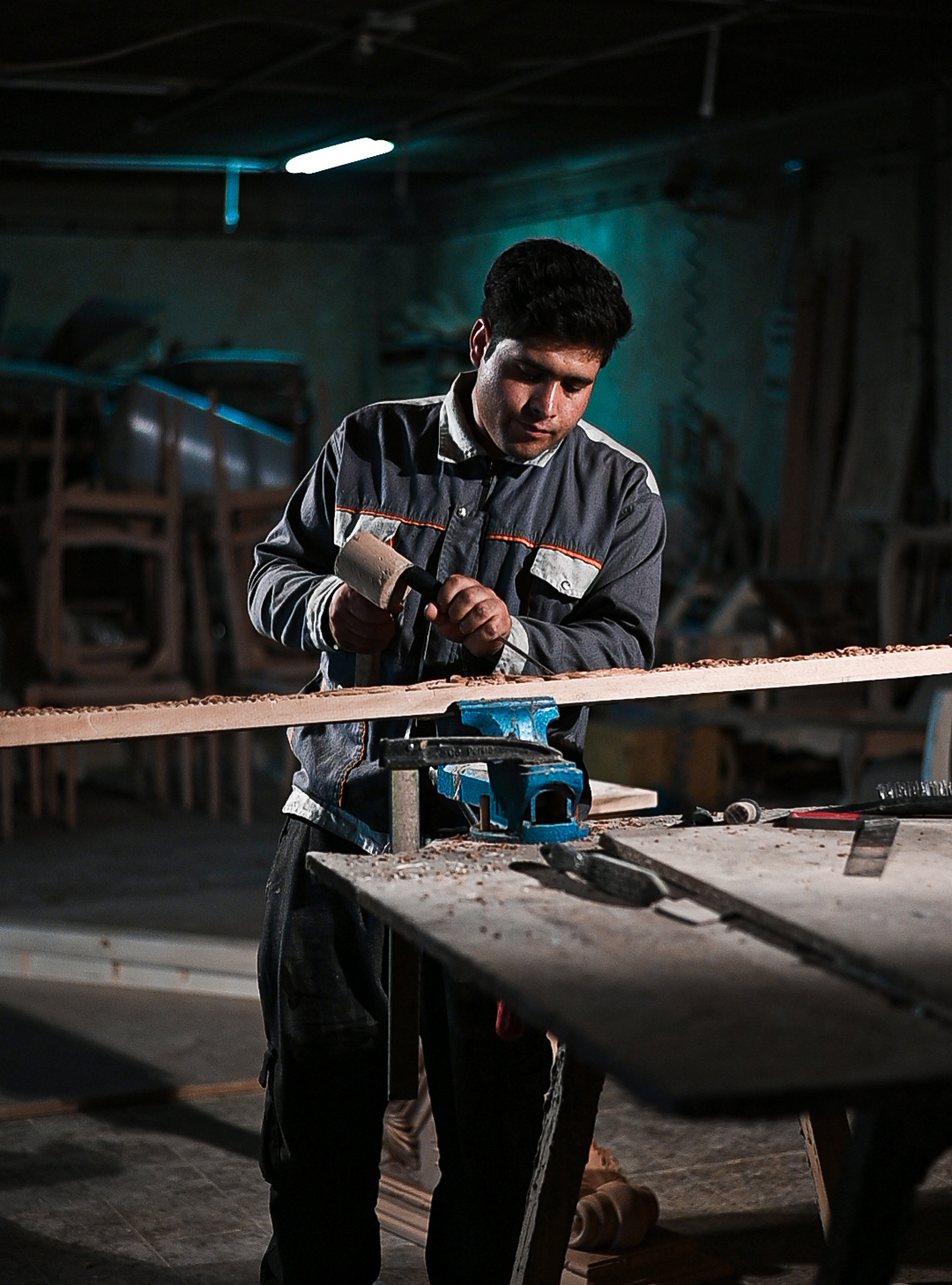 Craftsperson shaping a long wooden strip in a vise; fine shavings; key light on hands.