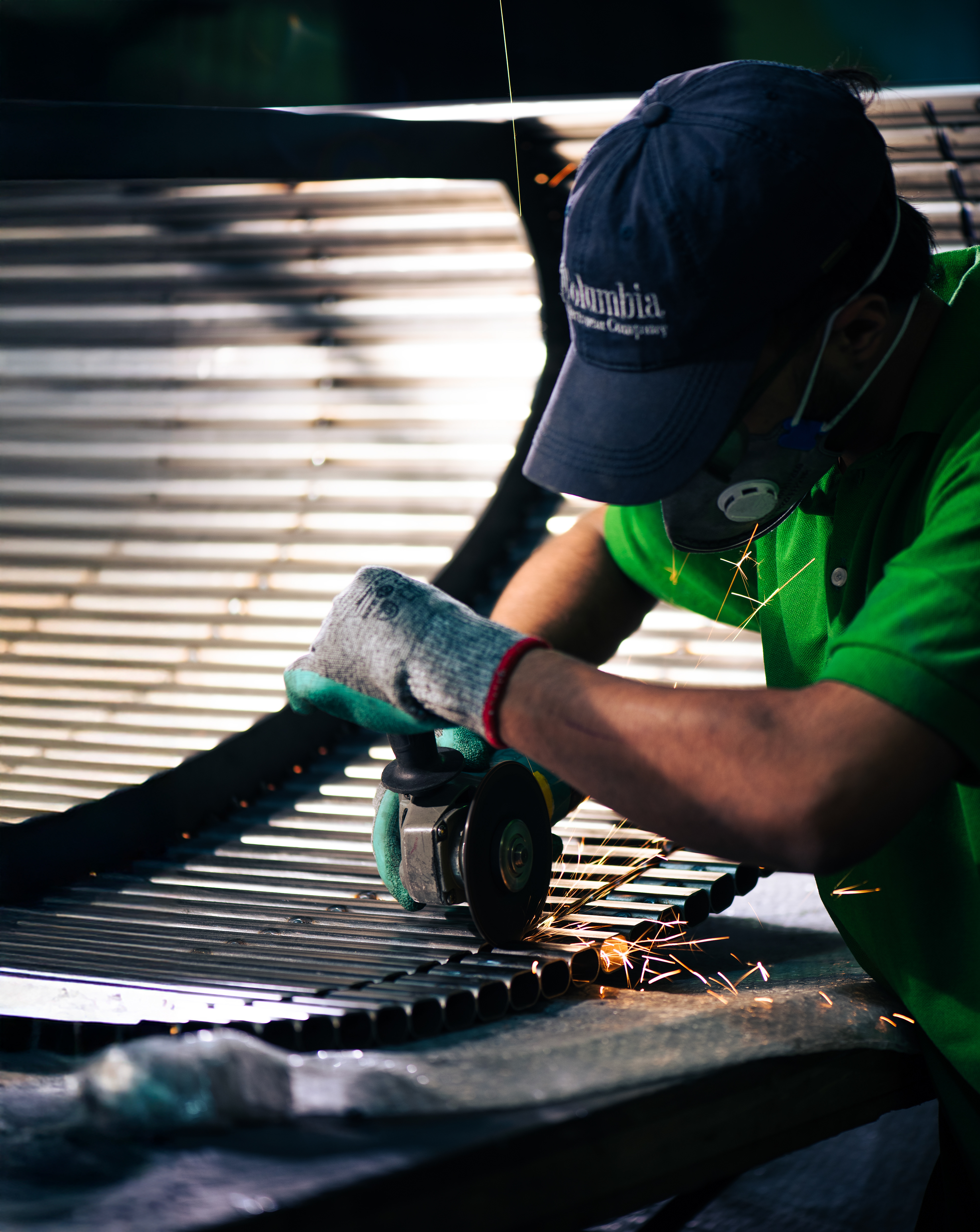 Grinder on ribbed metal tubes; orange sparks; gloves and respirator visible.
