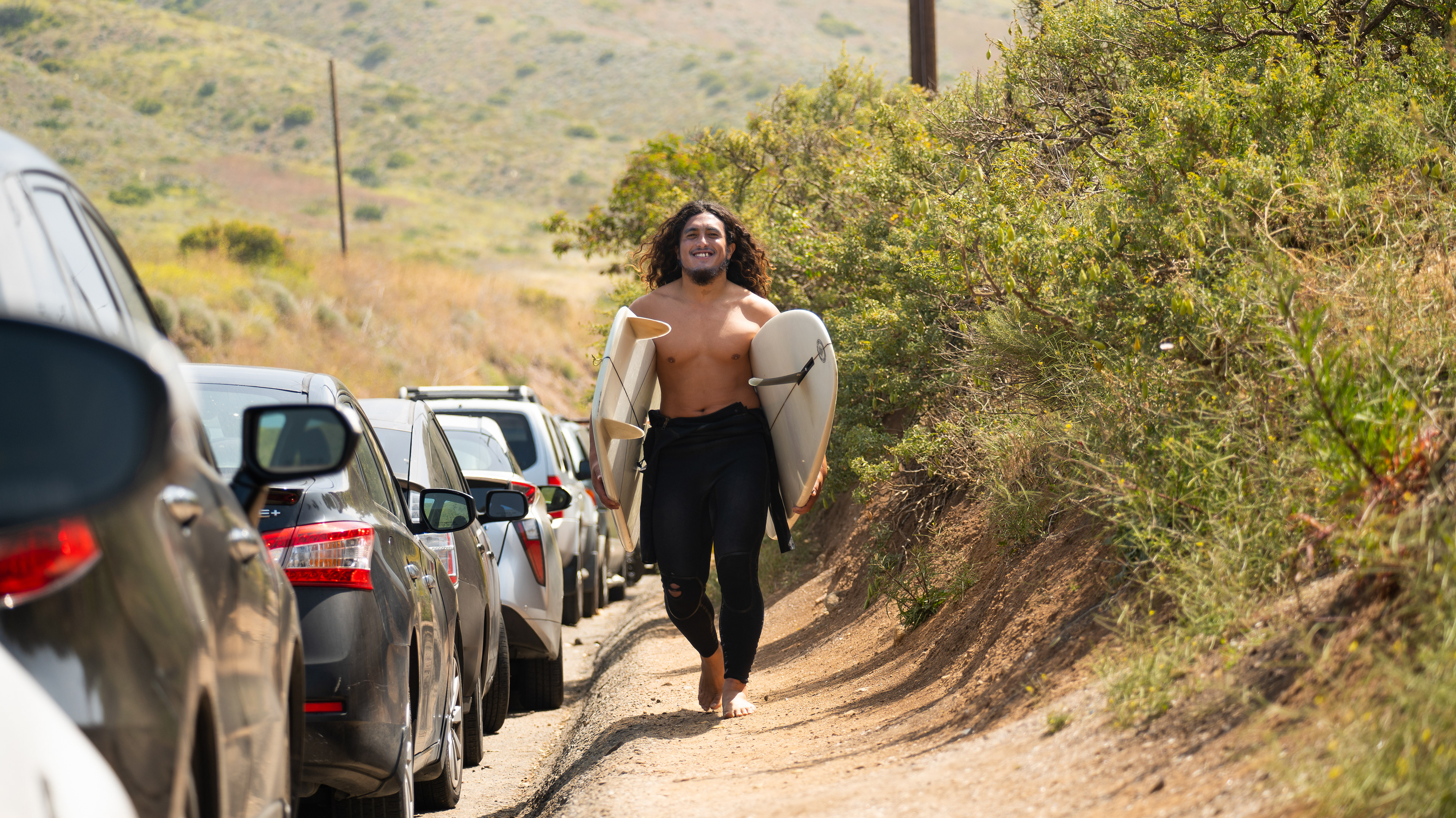 Murphy walking a dirt path next to Pacific Coast Highway on his way to surf in Malibu, California. Shot May 5, by DEVON JAMES.