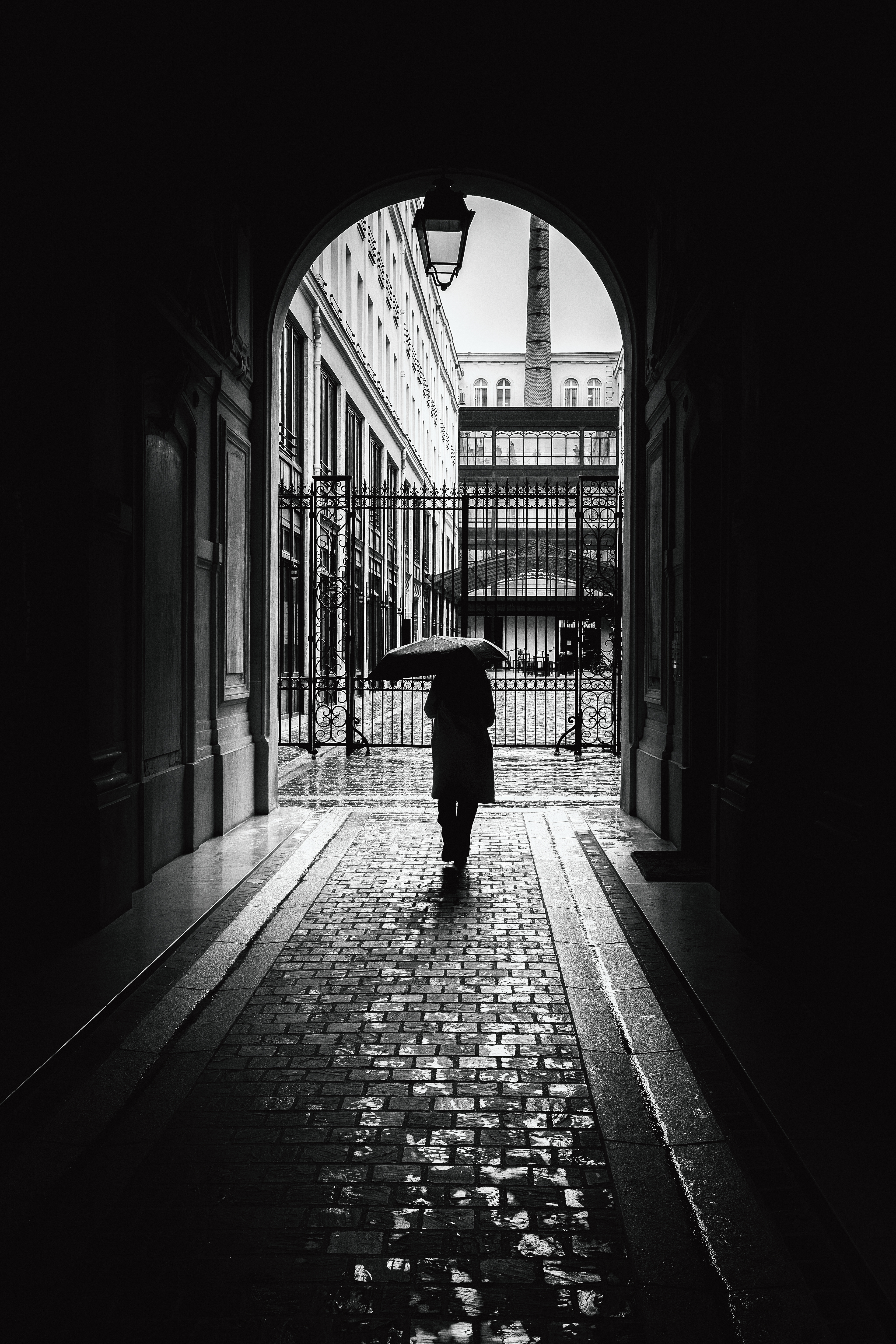 Person with an umbrella framed by a Paris archway.