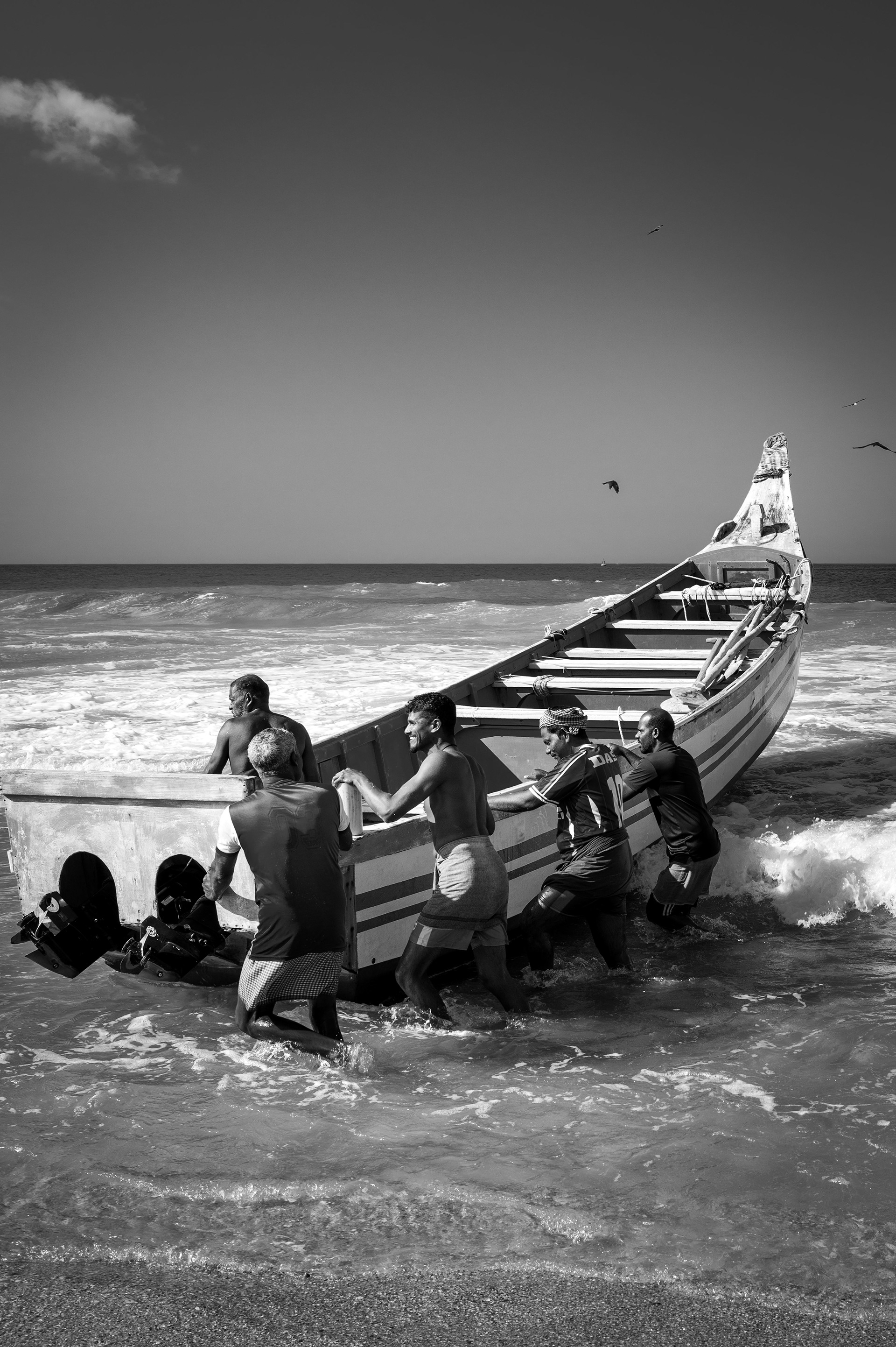 Fishermen bringing a wooden boat ashore in Kerala, India.
