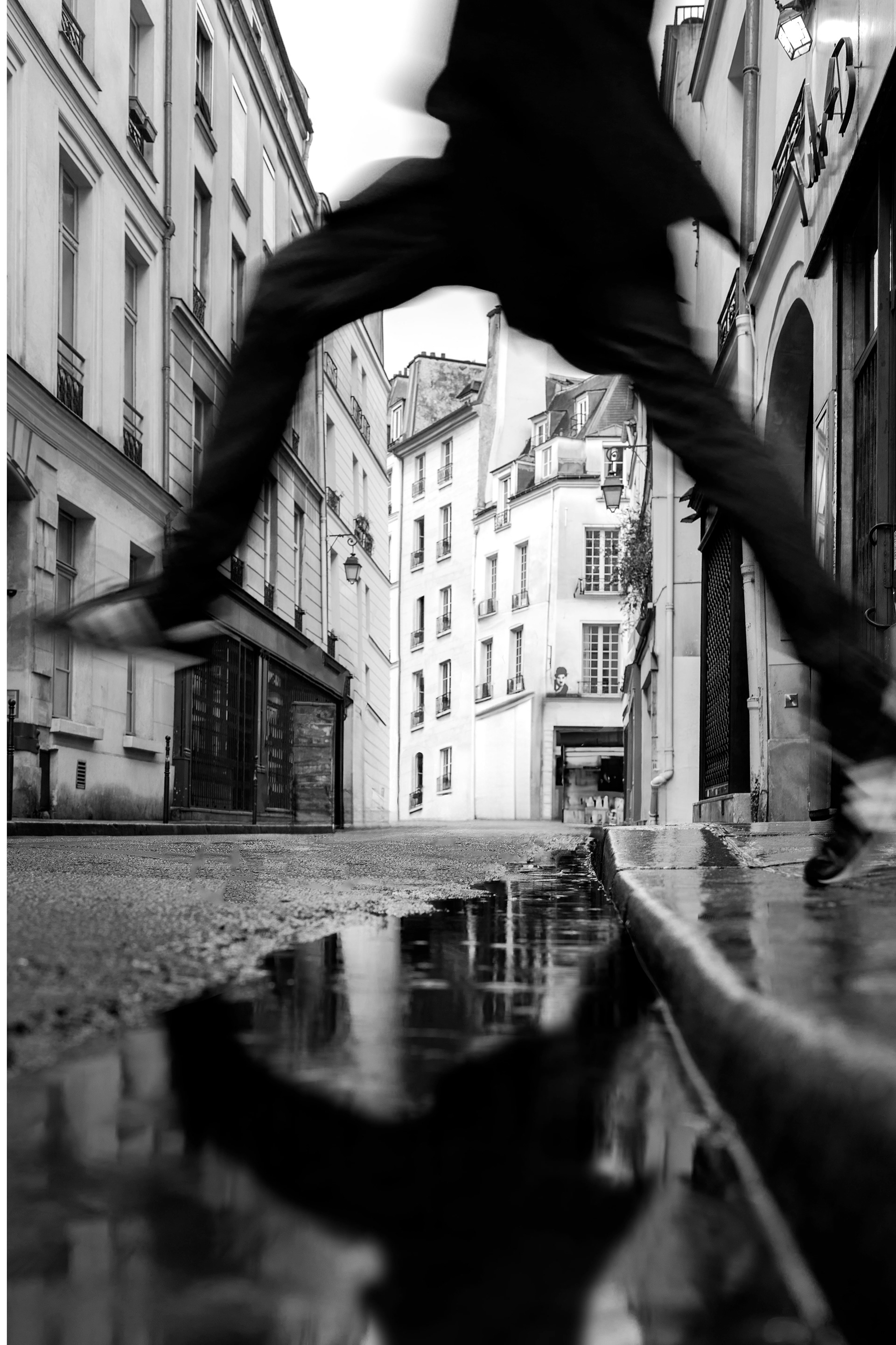 Blurred pedestrian reflected in a puddle in the Marais, Paris.