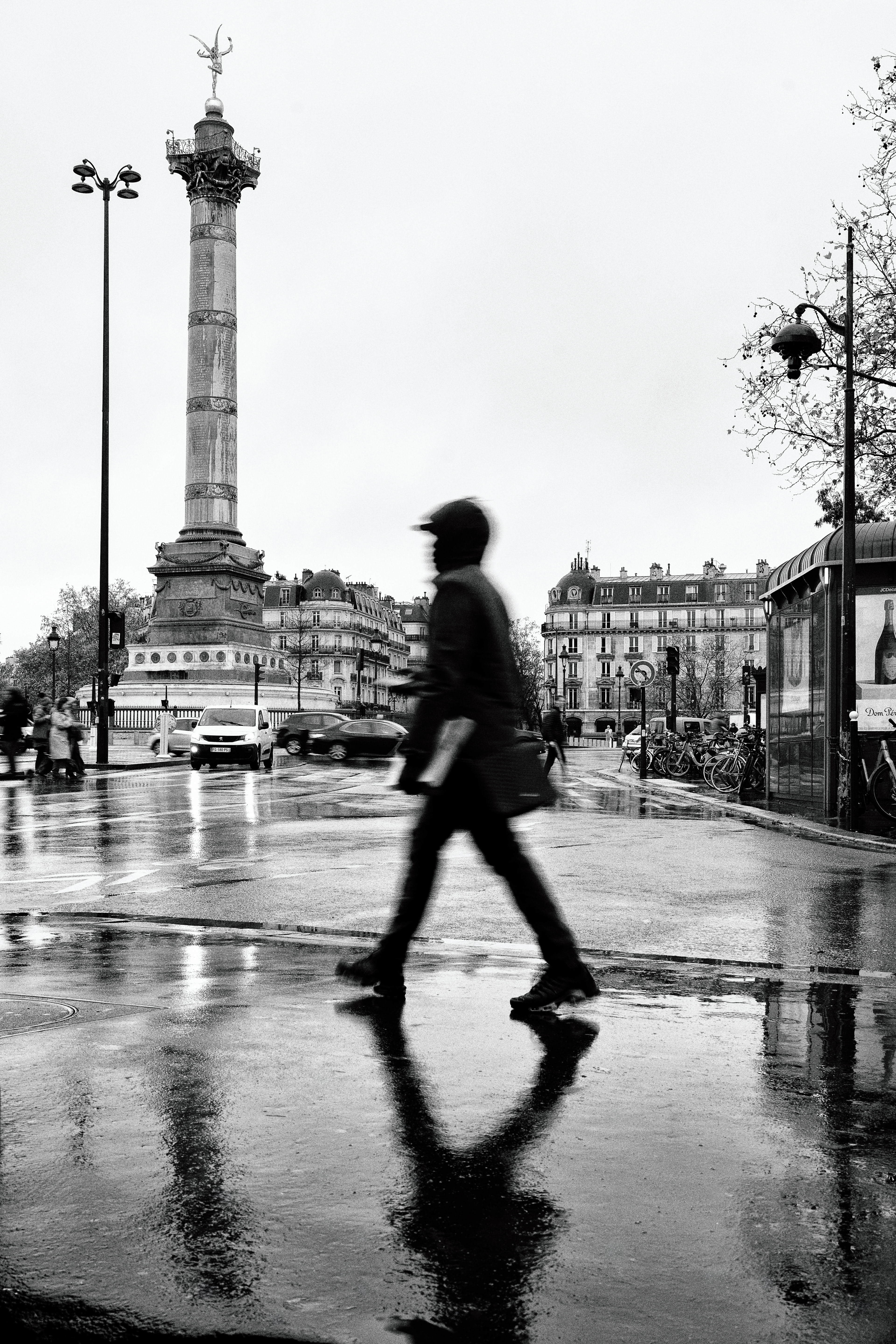 Pedestrain crossing Place de la Bastille on a rainy day in Paris.