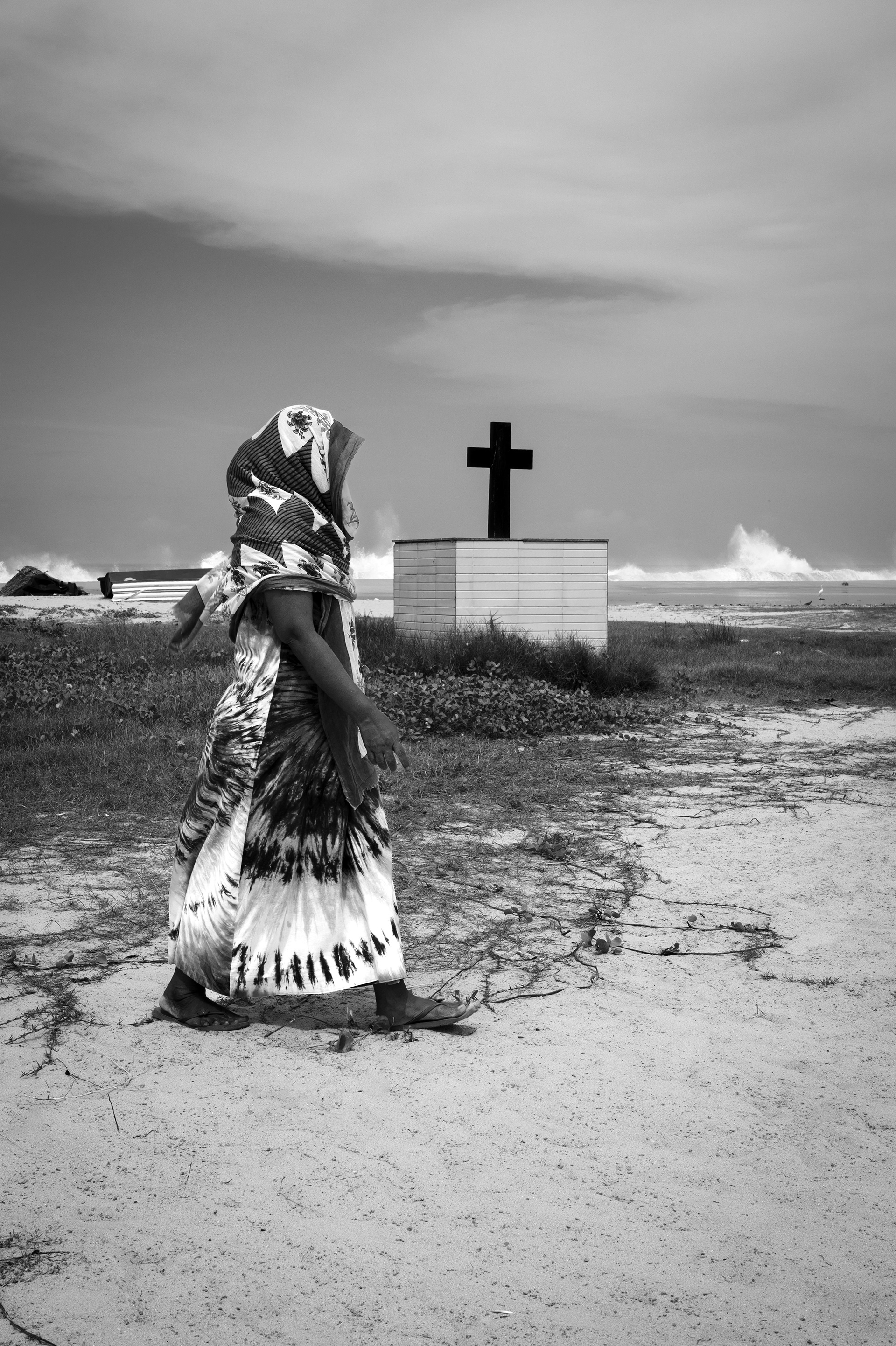 Woman walking past a cross on the Kerala coast, India.
