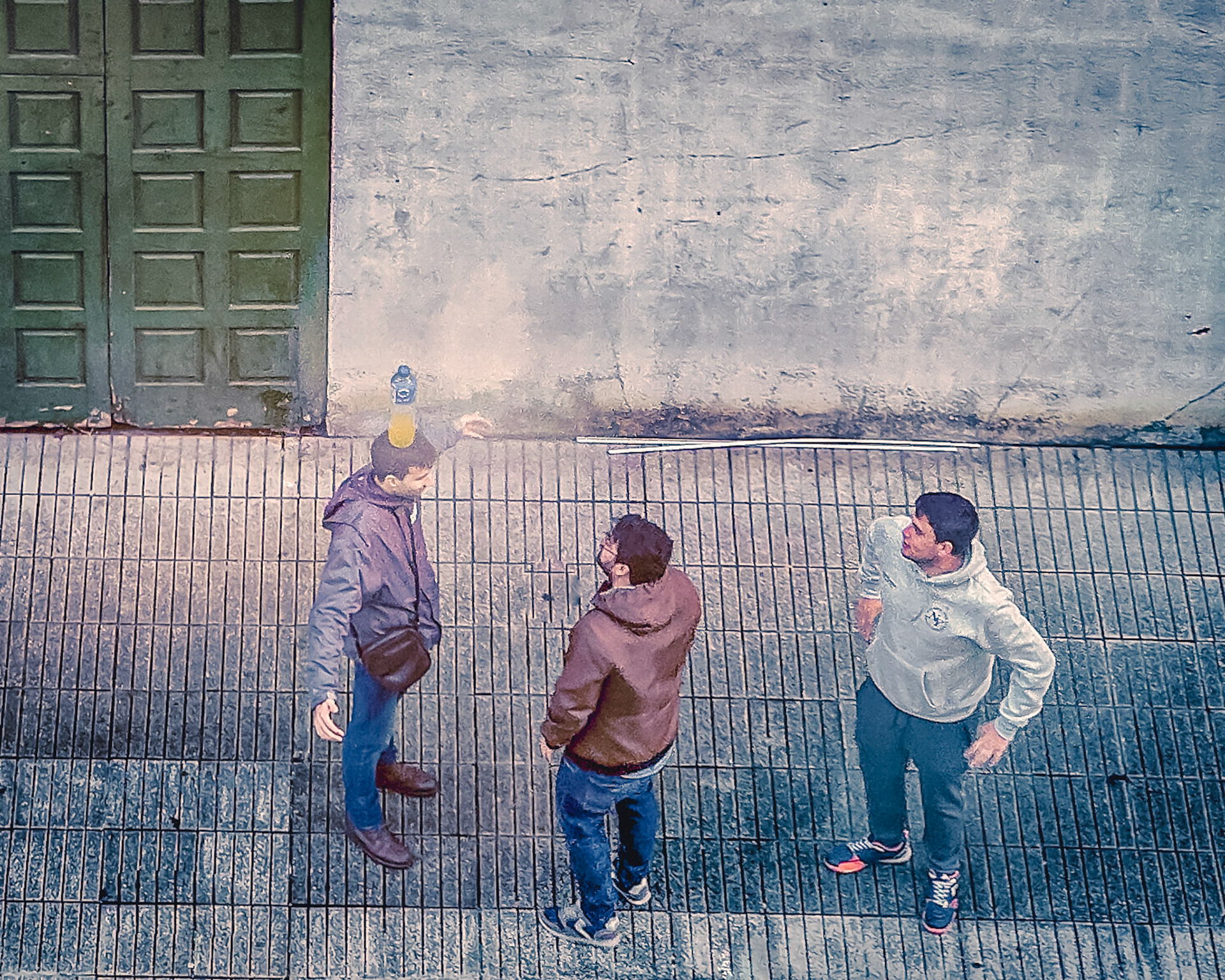 Tres mozos parolan na rúa baixo unha botella de refresco. Fotografía realizada con móbil desde unha posición cenital.