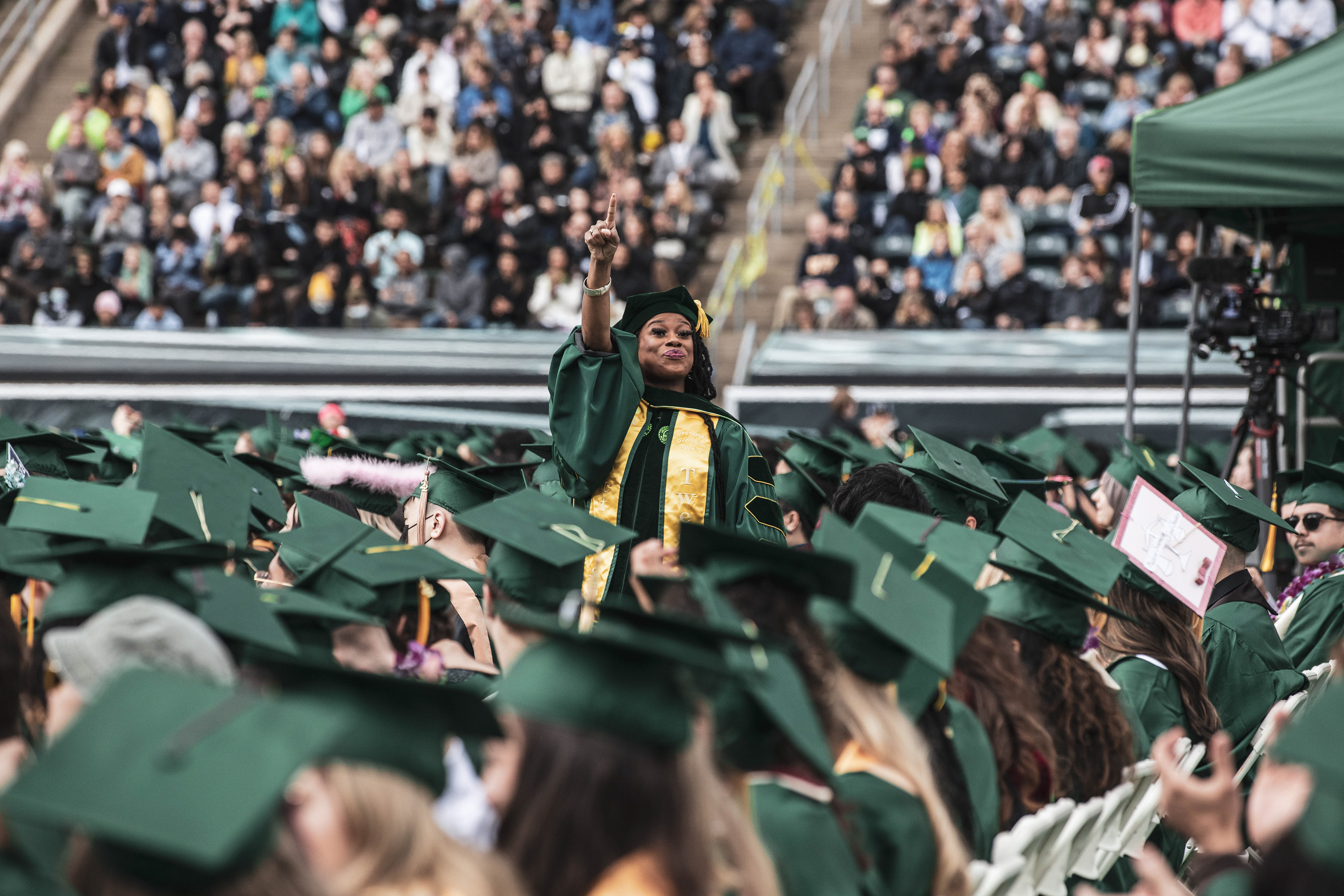 An individual graduating with a doctorate waves to members of the crowd. University of Oregon holds its 2022 Commencement Ceremony at Autzen Stadium in Eugene, Ore., on June 13, 2022. (Maddie Stellingwerf/Emerald)