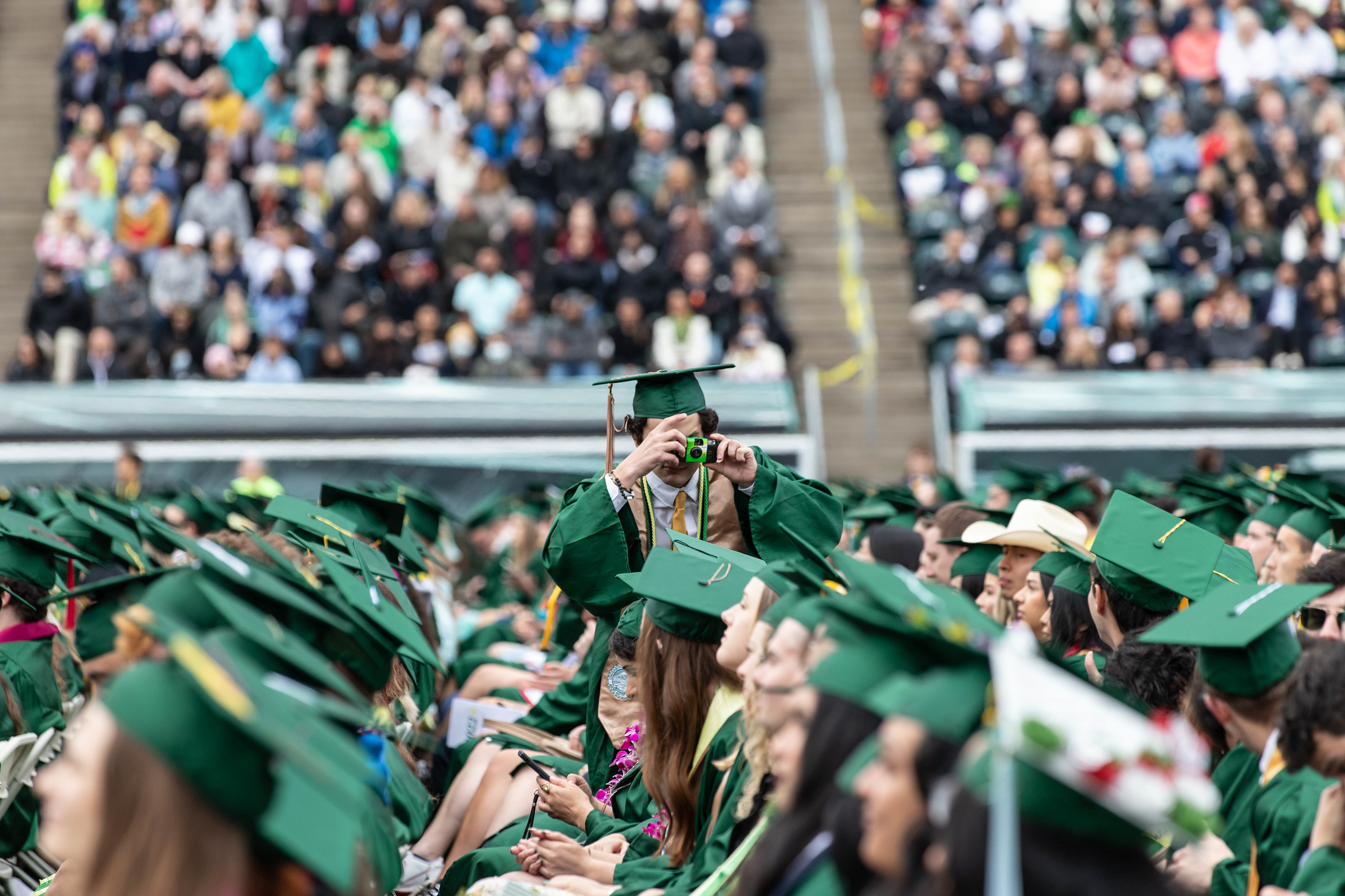 A graduate takes a photo of his fellow classmates on a disposable film camera. University of Oregon holds its 2022 Commencement Ceremony at Autzen Stadium in Eugene, Ore., on June 13, 2022. (Maddie Stellingwerf/Emerald)