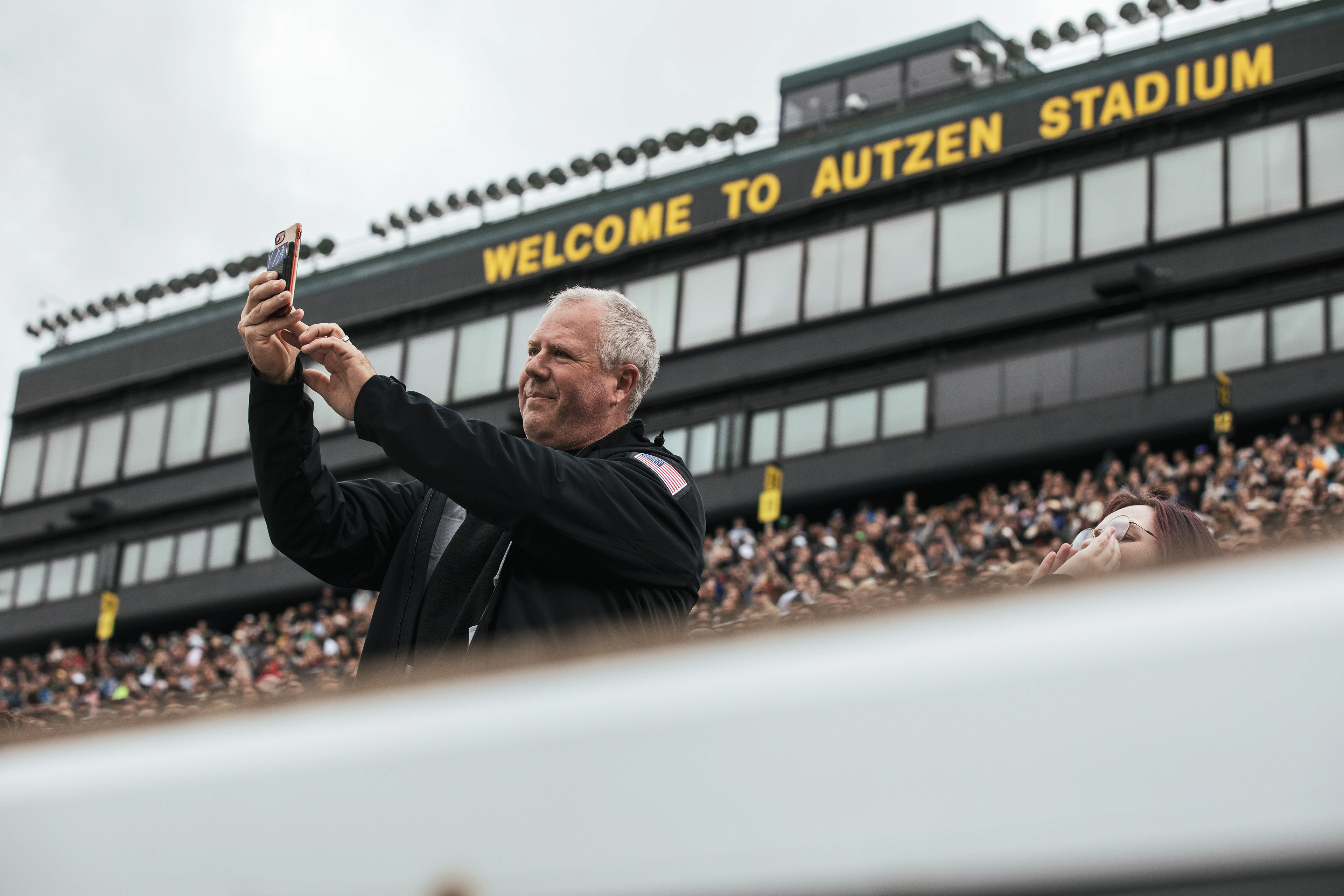 A member of the crowd takes a photo of graduates as they are called to stand. University of Oregon holds its 2022 Commencement Ceremony at Autzen Stadium in Eugene, Ore., on June 13, 2022. (Maddie Stellingwerf/Emerald)