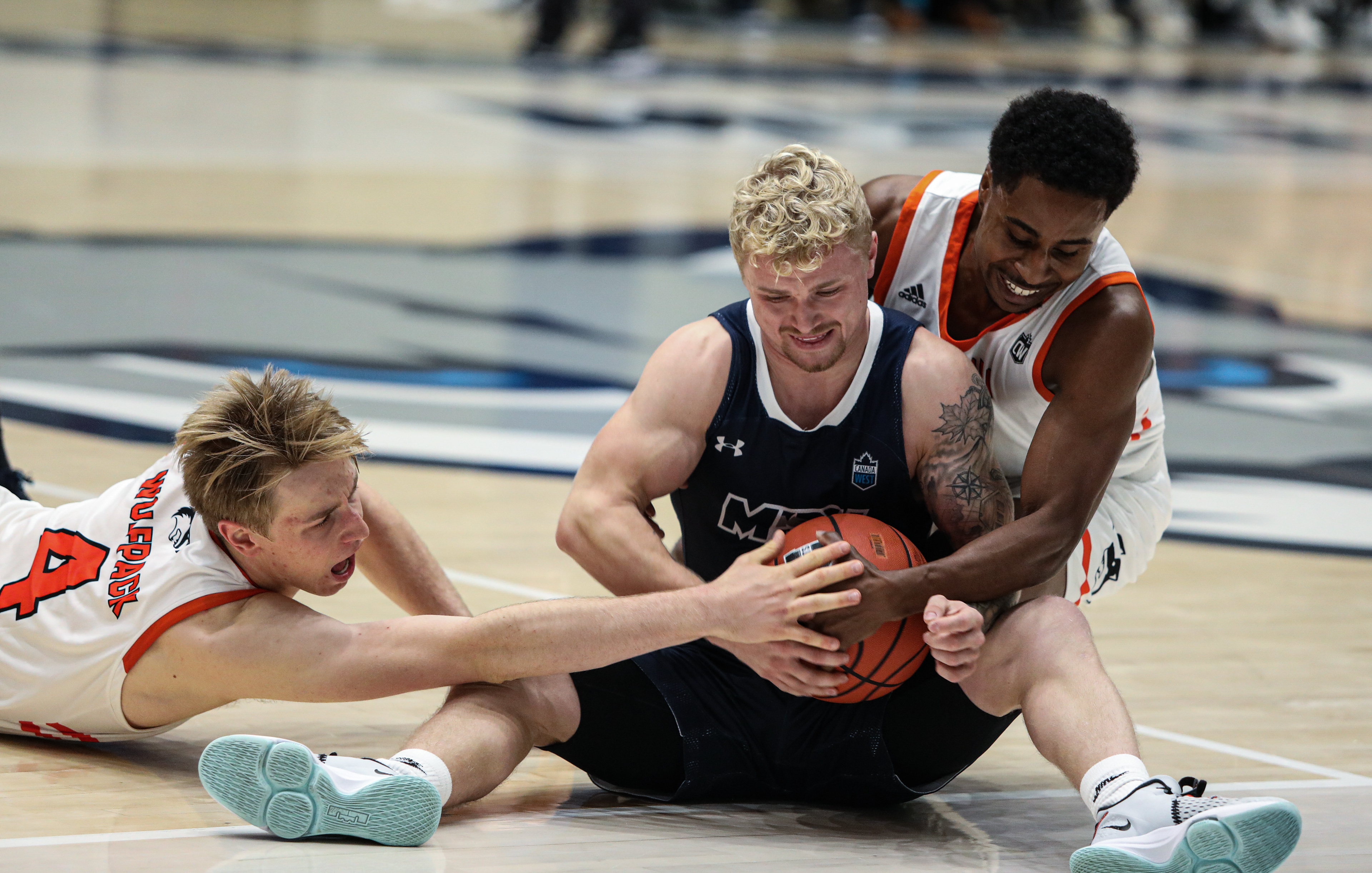 Thompson Rivers University Wolfpack 's two players fight for the ball with Mount Royal University Cougars guard Matt Fullerton, center, at the Mount Royal gymnasium in Calgary on Friday, Oct. 15, 2021. The Cougars beat the Wolfpack by a score of 67-66 in Alberta Colleges Athletic Conference men’s basketball action.
