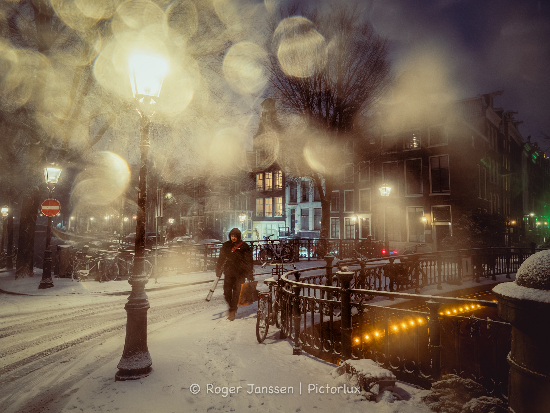 A pedestrian struggling through a blizzard during blue hour on the canals in Amsterdam.