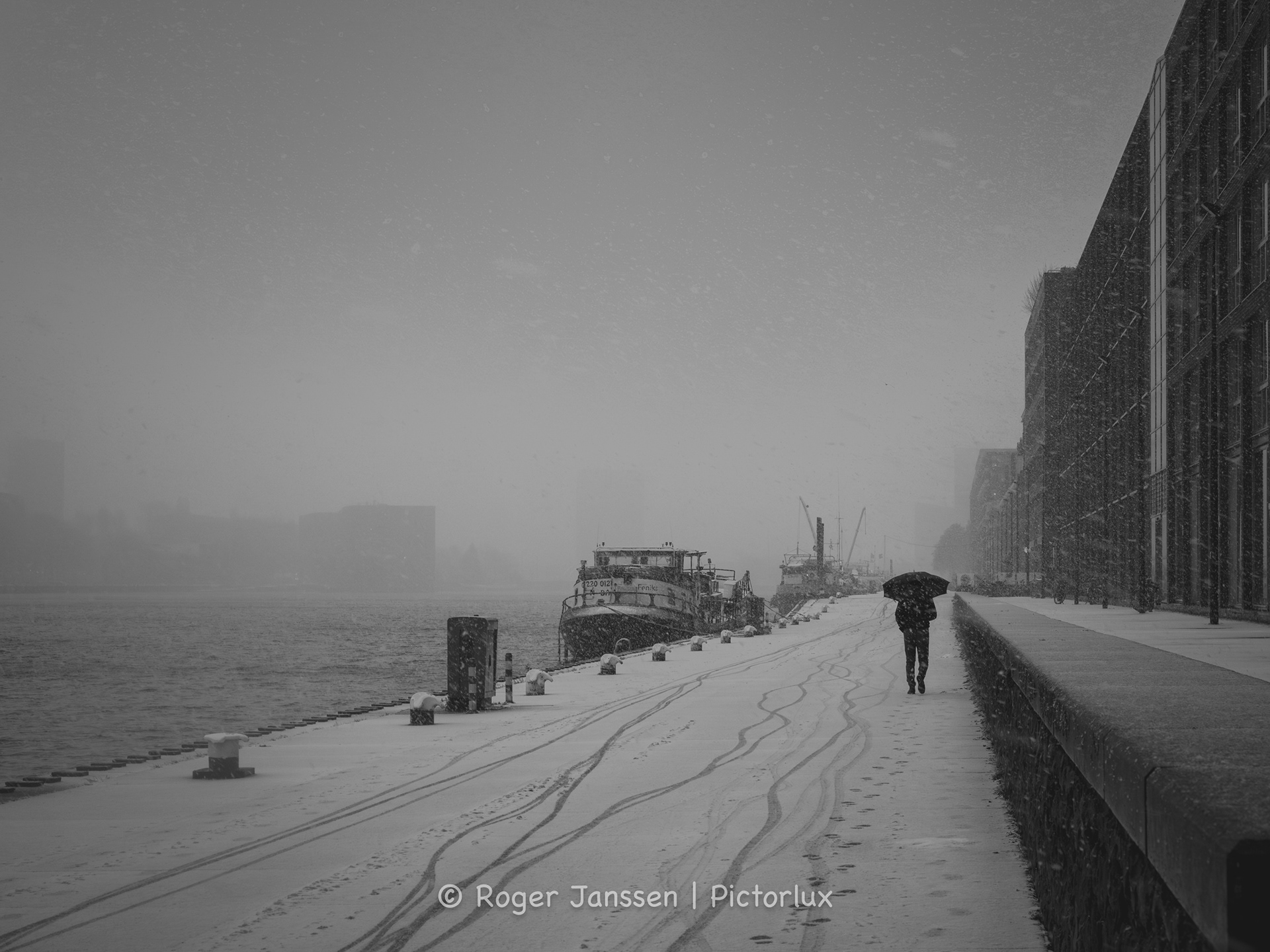 Eenzame wandelar op de Veemkade in Amsterdam die zich een weg baant door een sneeuwbui.