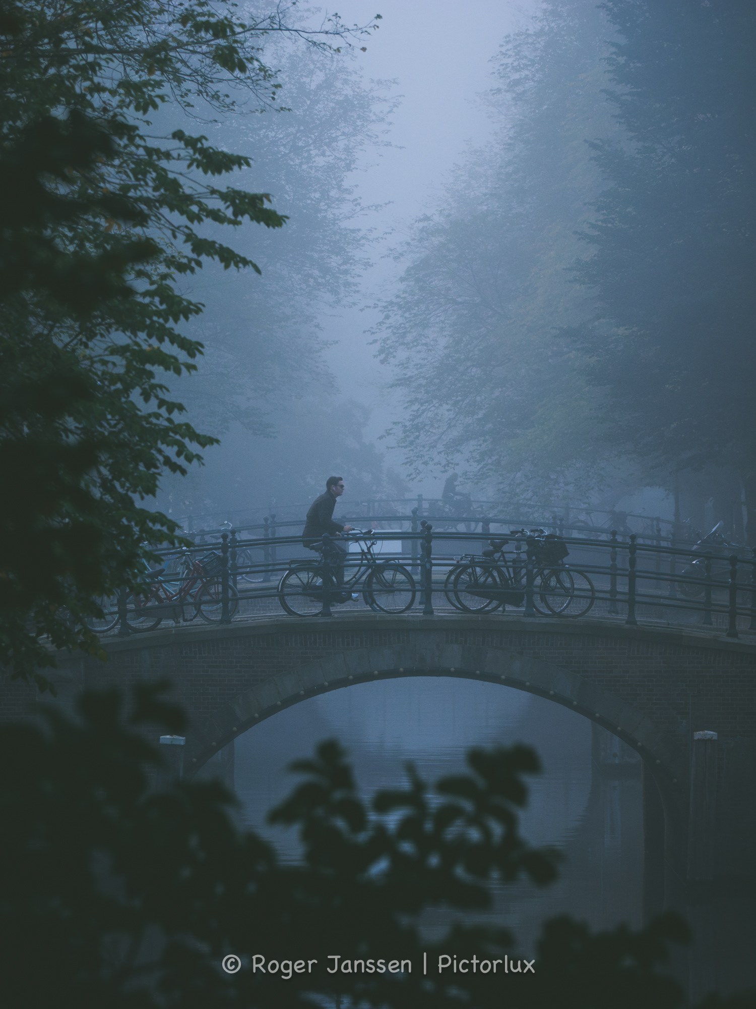 Commuting cyclist crossing a canal bridge in Amsterdam on a foggy morning.