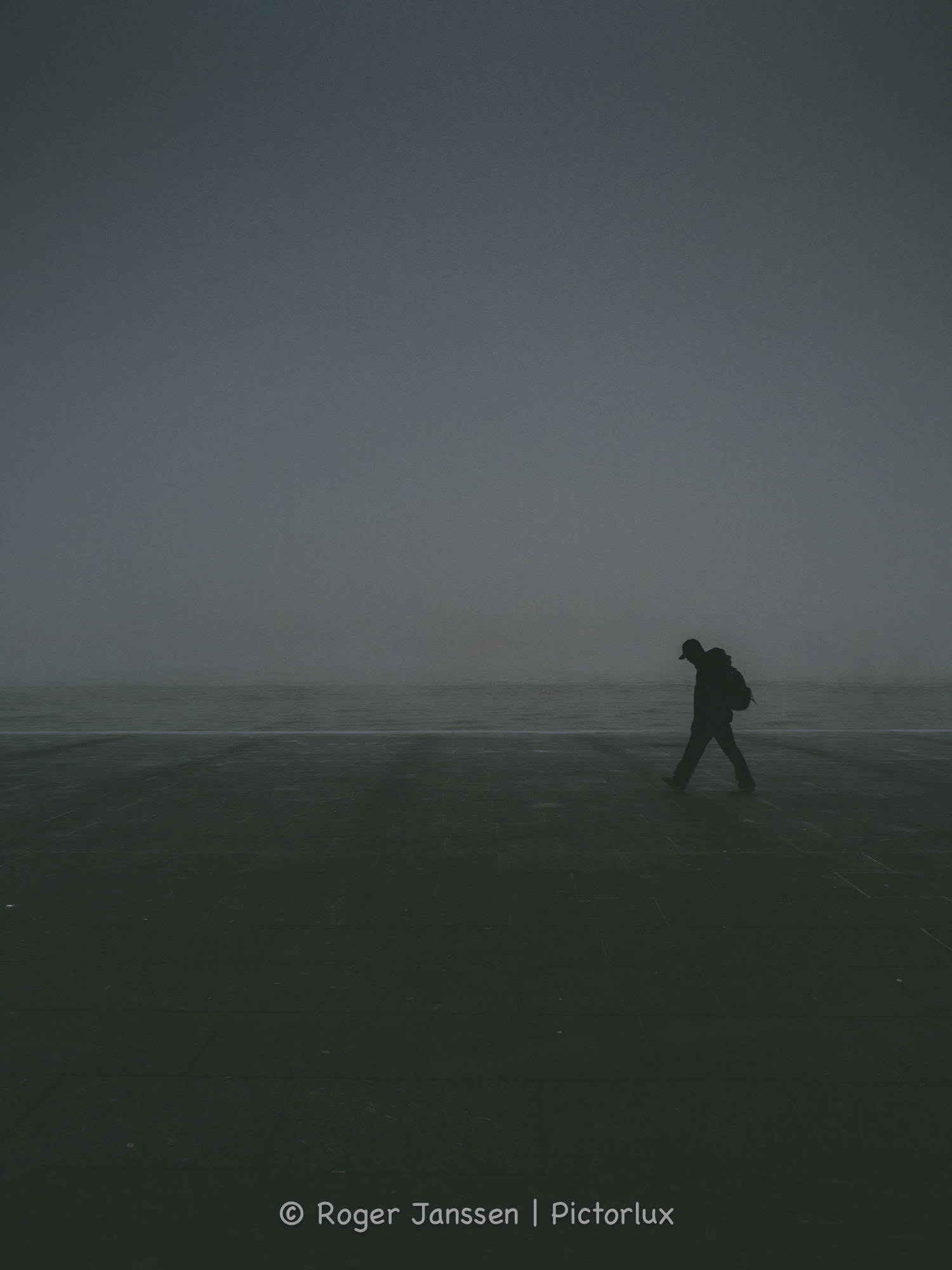 Lone pedestrian near the IJ river in a desolate Amsterdam on a cold foggy morning.