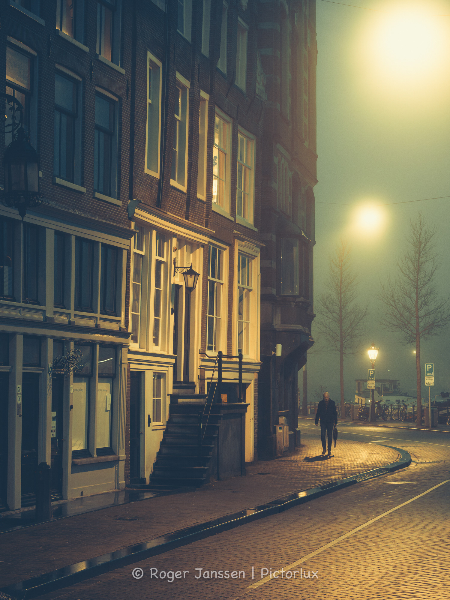 Lonely pedestrian walking near the Amstel river in Amsterdam on a foggy morning.