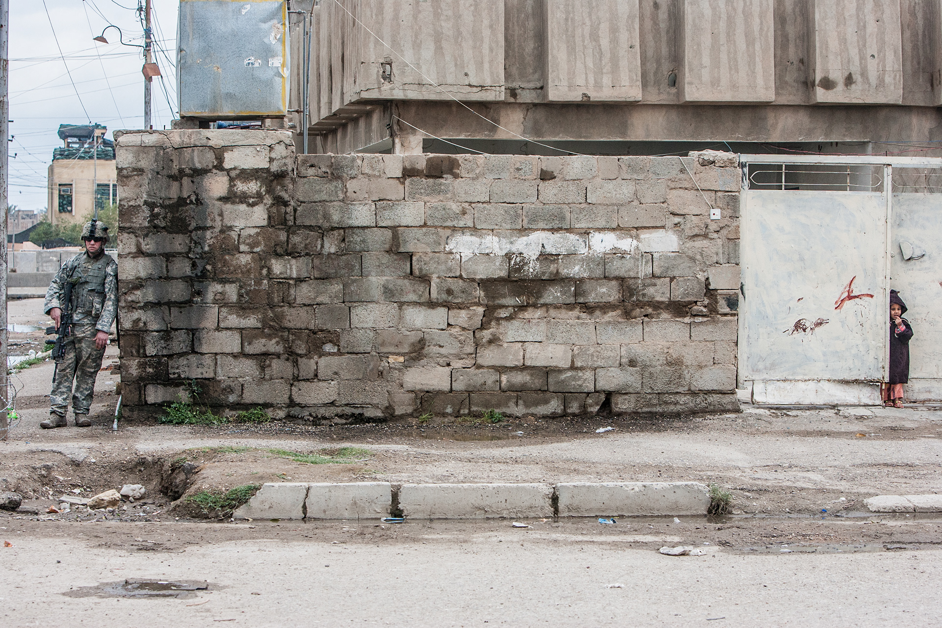 American soldier on patrol as a local Iraqi girl looks on in Ramadi.