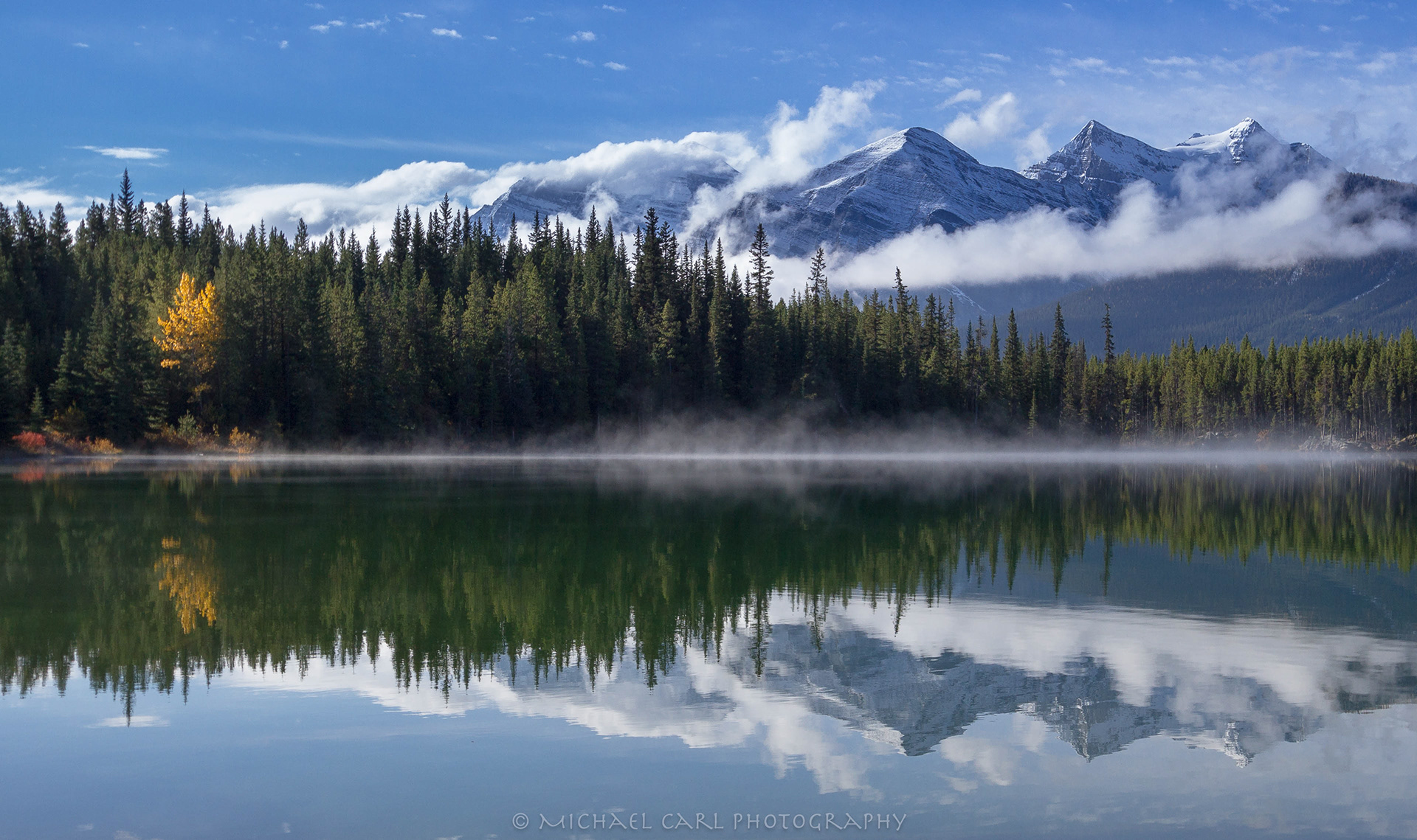 Landscape photograph of the Waputik Mountain Range reflecting off Herbert Lake in Banff National Park Canada.