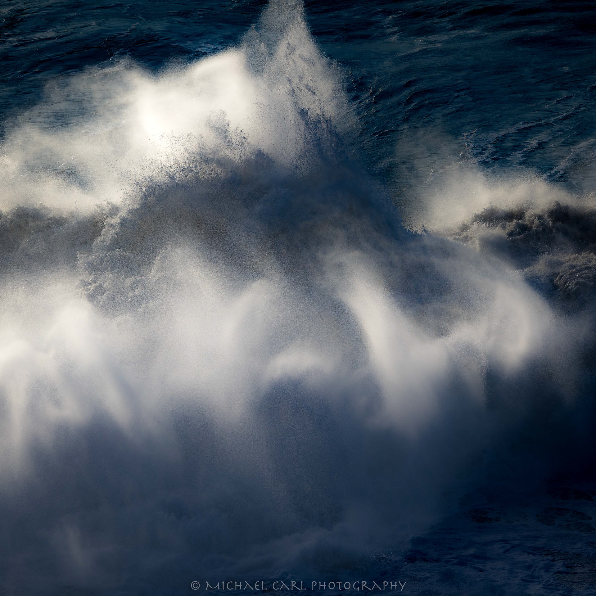 Seascape photography of crashing wave as the low angle of the sun creates highlights in the ocean mist.